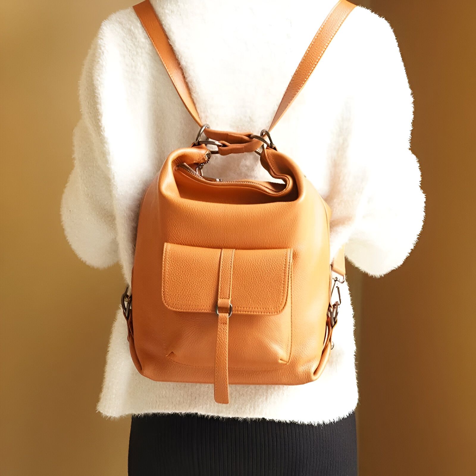 Un sac à dos en cuir brun porté par une femme en pull blanc.