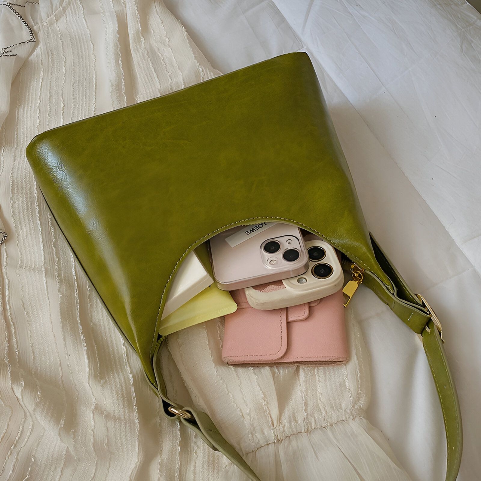 Un sac à main vert foncé avec une sangle et une fermeture éclair dorée, ouvert pour révéler un téléphone portable et un portefeuille.