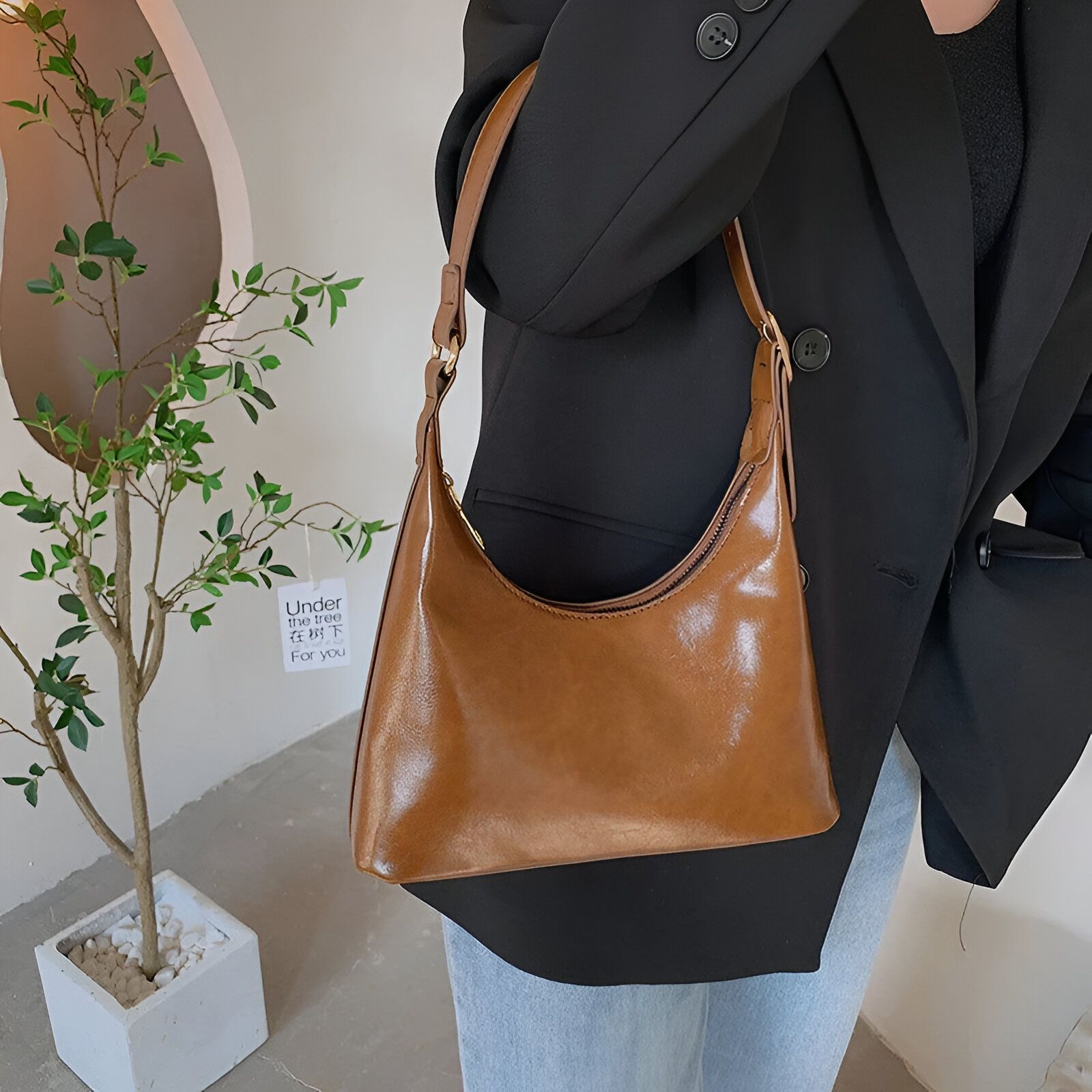 Un sac à main brun porté par une femme vêtue d'un blazer noir et d'un jean bleu.