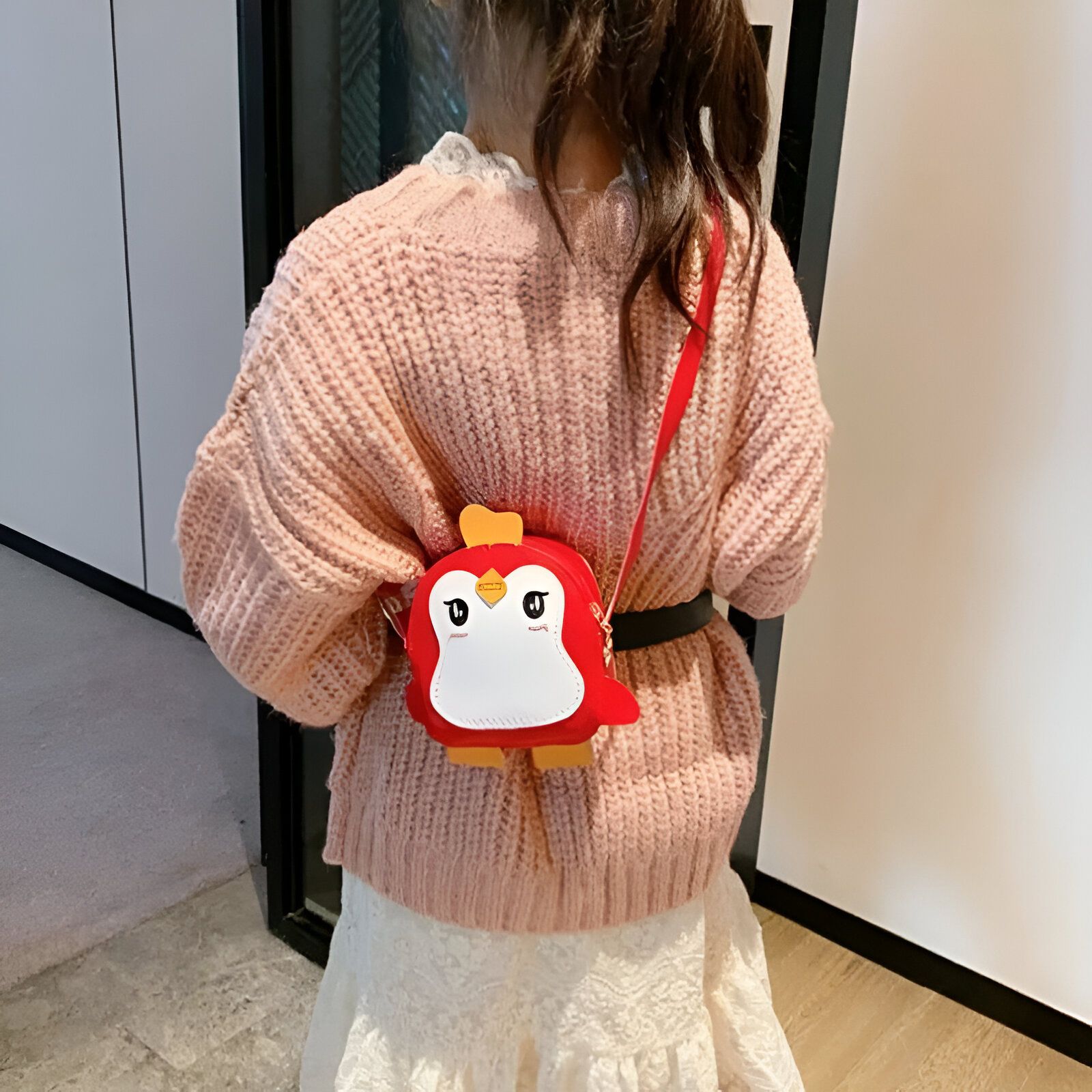 Une petite fille porte un sac à main rouge en forme de pingouin.