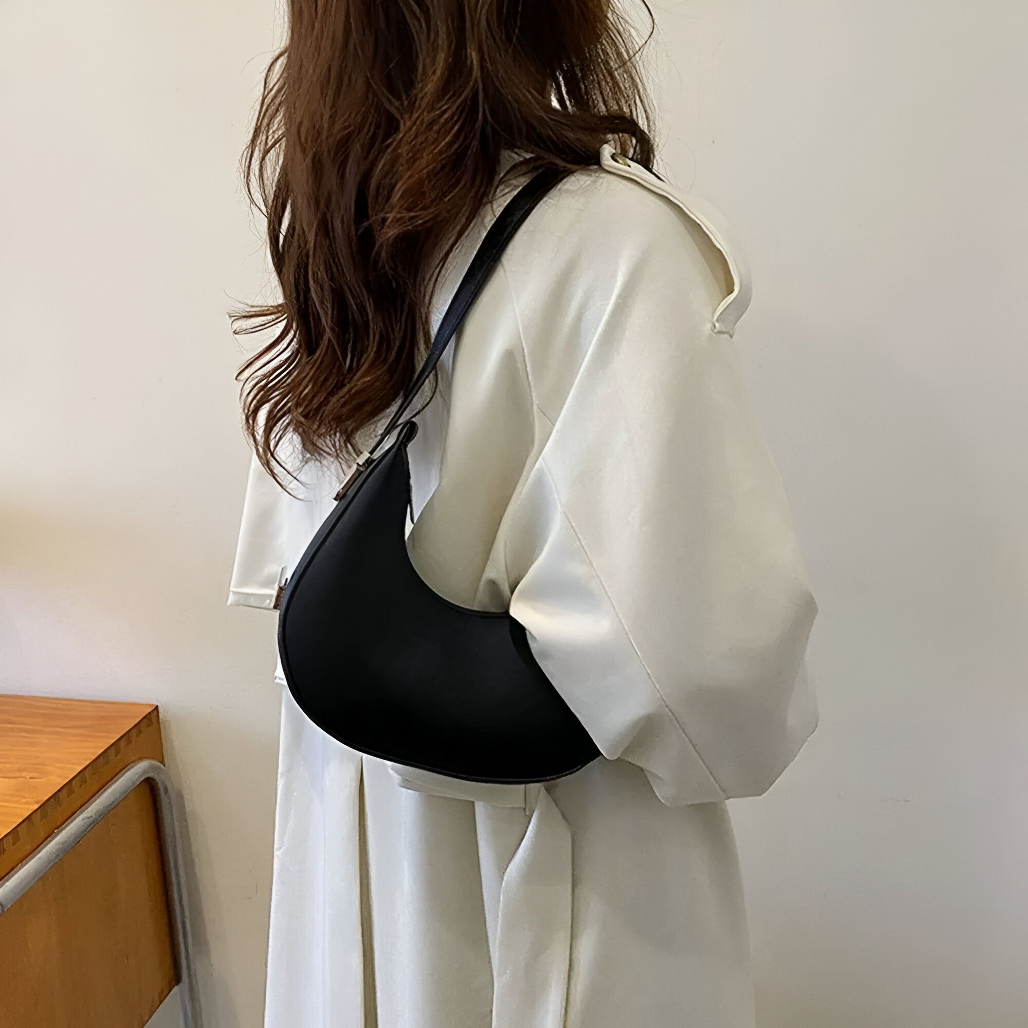 Une femme portant un chemisier blanc et un sac à main noir en forme de croissant de lune.