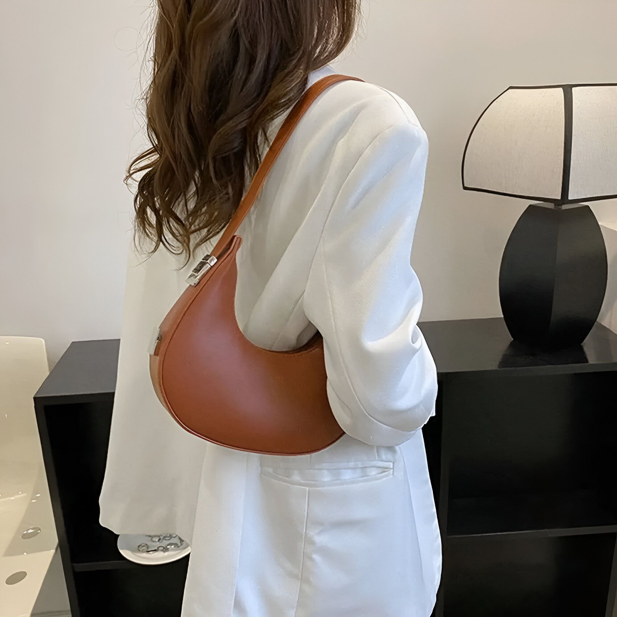 Une femme portant un blazer blanc et un sac à main marron en forme de croissant de lune.