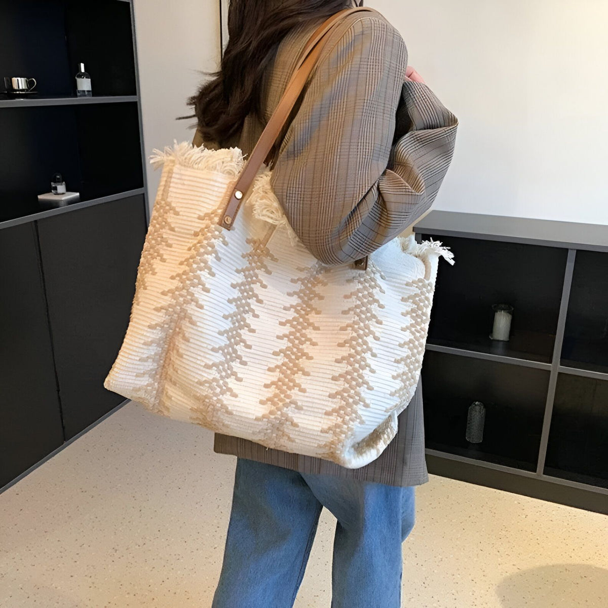 Une femme porte un grand sac à main en tissu blanc avec des motifs marrons. Le sac est porté à l&#39;épaule et a des anses en cuir marron.