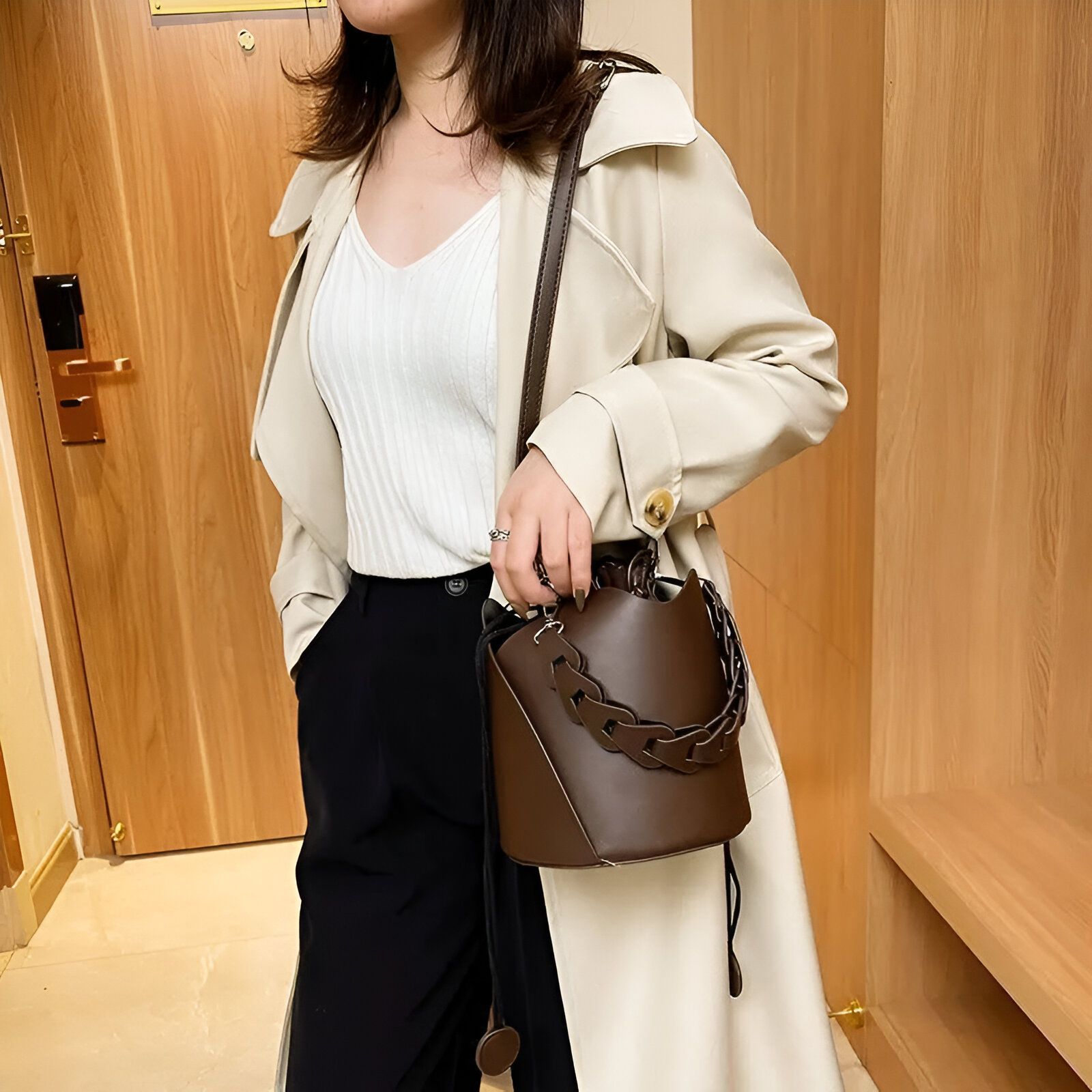 Une femme portant un manteau beige et un sac à main brun en forme de seau avec une chaîne.