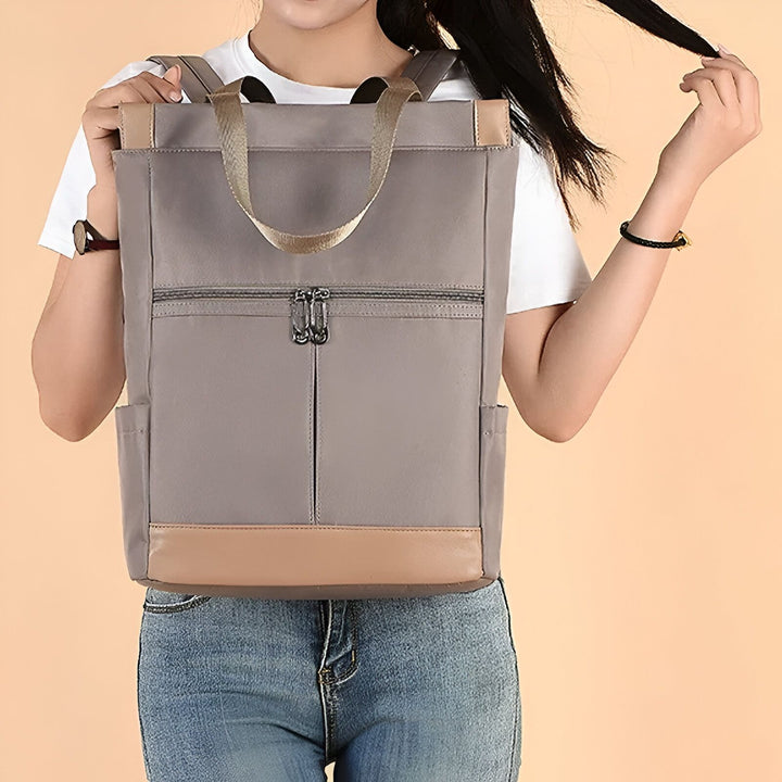 Personne portant un sac à dos gris avec détails marron clair et bretelles dorées., 46193874665696,46193874698464,46193874731232,46193874764000