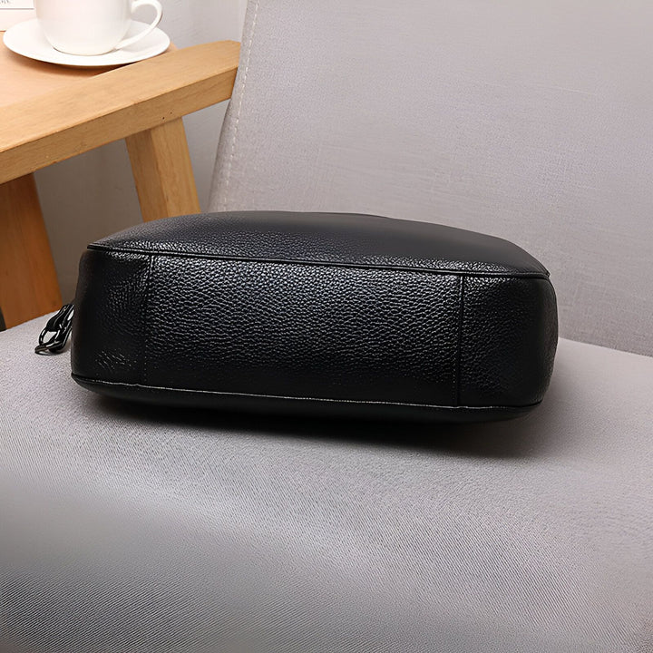Sac noir en cuir grainé posé sur un siège gris., 46193845993696,46193846026464,46193846059232,46193846092000,46193846124768
