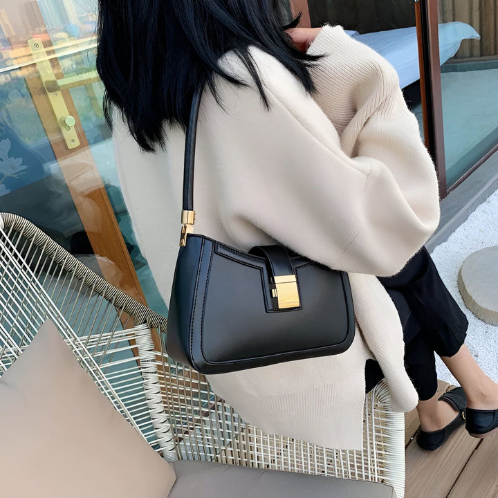 Femme portant un sac à main noir avec fermoir doré, assise sur une chaise., 46193936236768,46193936269536,46193936302304,46193936335072