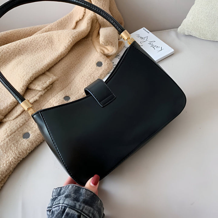 Sac baguette noir brillant tenu par une main devant une veste beige., 46193936236768,46193936269536,46193936302304,46193936335072