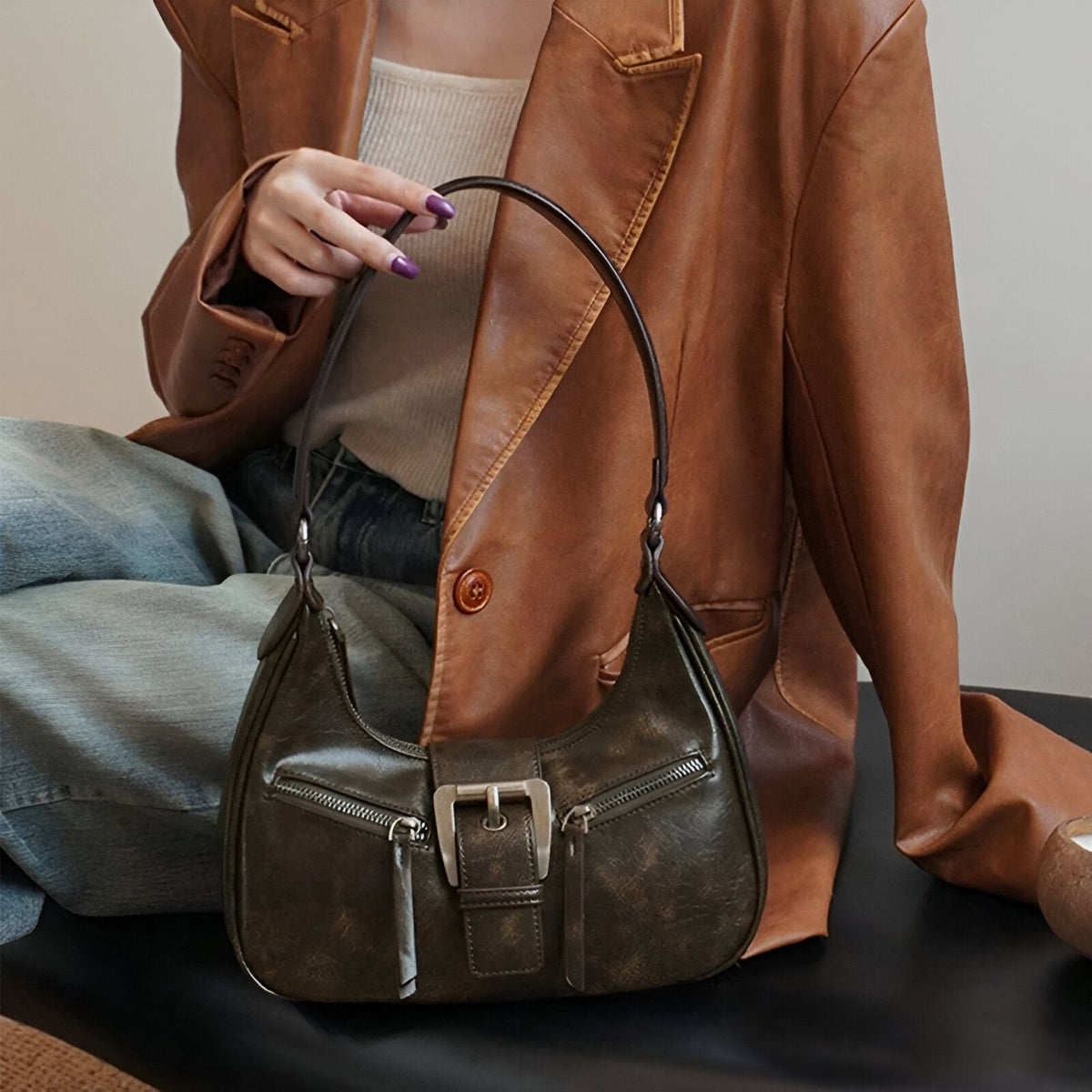 Un sac à main en cuir marron foncé avec une boucle argentée.  Le sac est porté par une femme vêtue d&#39;une veste en cuir brun.