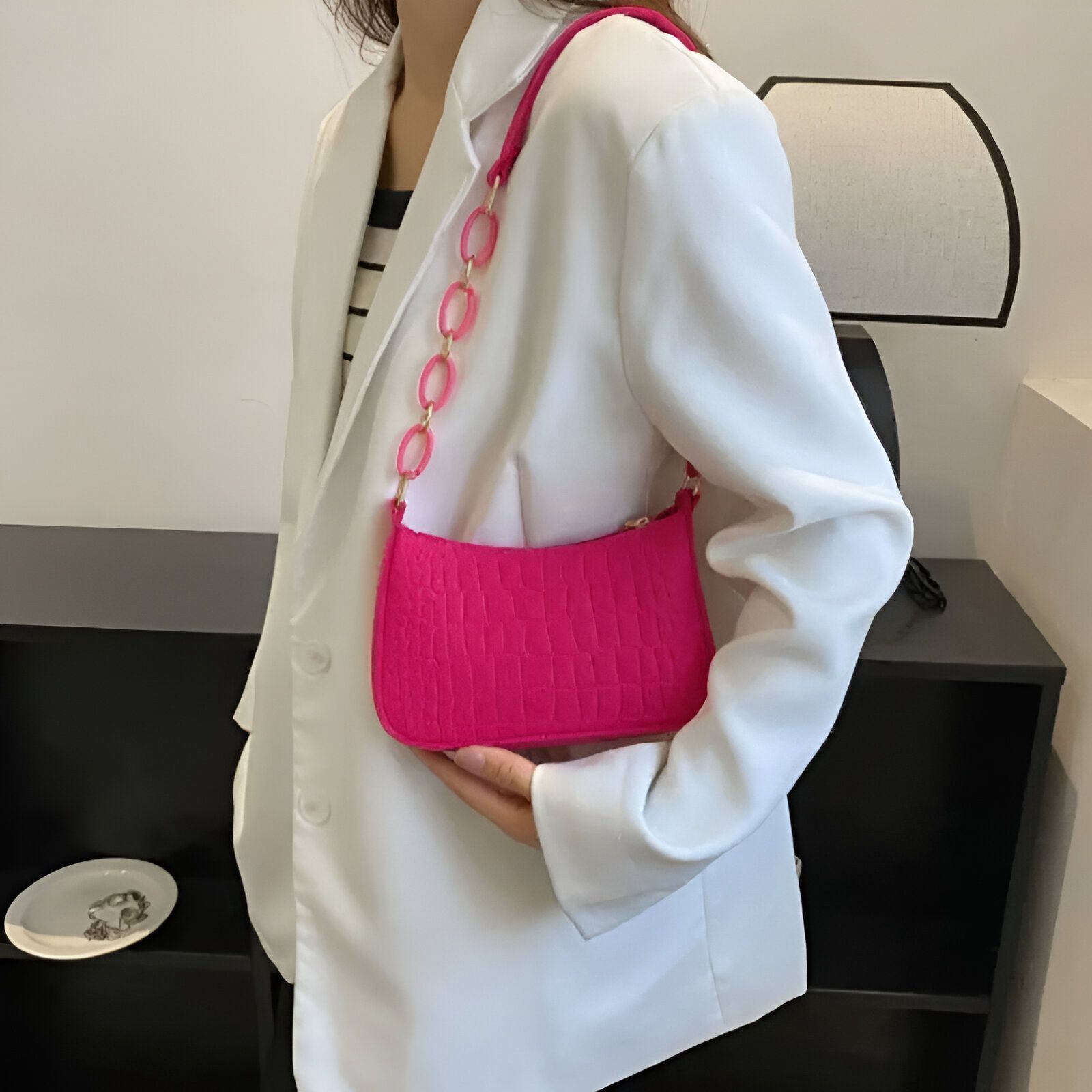 Un sac à main rose vif avec une chaîne dorée porté par une femme en blazer blanc.