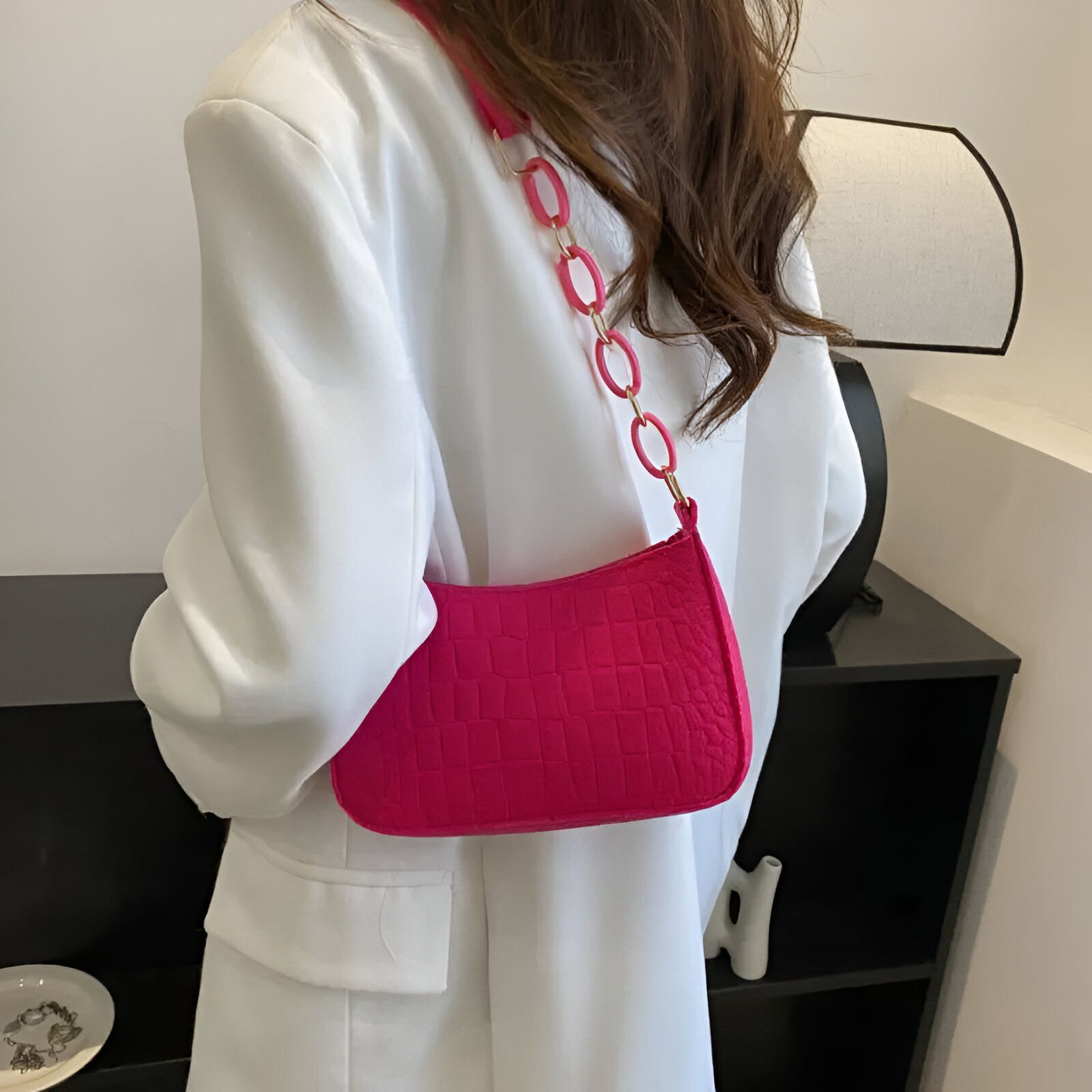 Un sac à main rose avec une chaîne dorée porté par une femme.