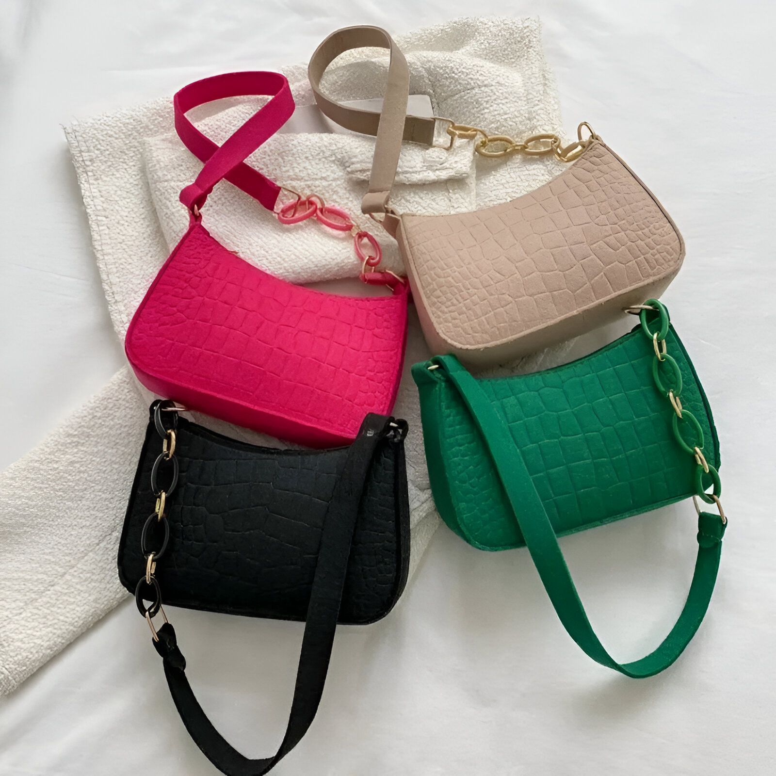 Quatre sacs à main en similicuir avec une texture de peau de crocodile dans différentes couleurs : rose, noir, beige et vert. Ils ont tous une chaîne dorée comme breloque et une bandoulière.