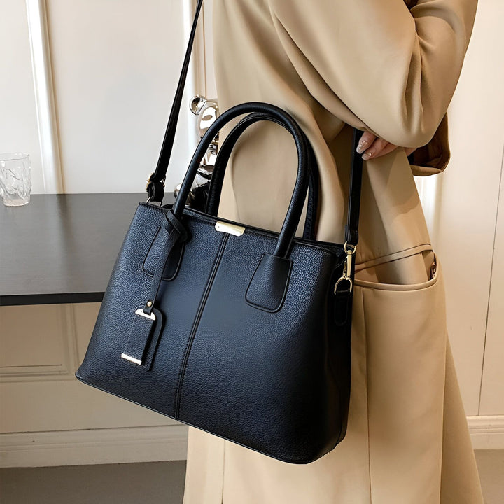 Sac à main noir en cuir avec anse et bandoulière, porté par une personne en manteau beige., 46194059018464,46194059051232,46194059084000,46194059116768,46194059149536