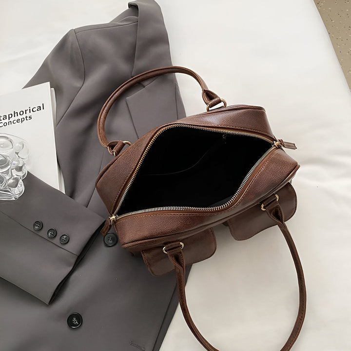 Sac à main en cuir marron ouvert, posé sur un blazer gris à côté d'un livre., 46193871290592,46193871323360,46193871356128,46193871388896