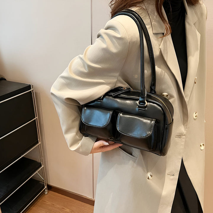 Sac à main noir brillant avec deux poches avant, porté par une personne., 46193871290592,46193871323360,46193871356128,46193871388896