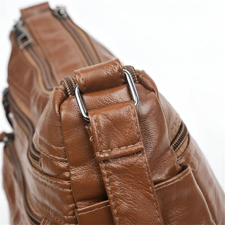 Détail d'une attache sangle en métal et cuir sur un sac en cuir marron avec fermetures éclair., 46194026643680,46194026676448,46194026709216,46194026741984,46194026774752,46194026807520
