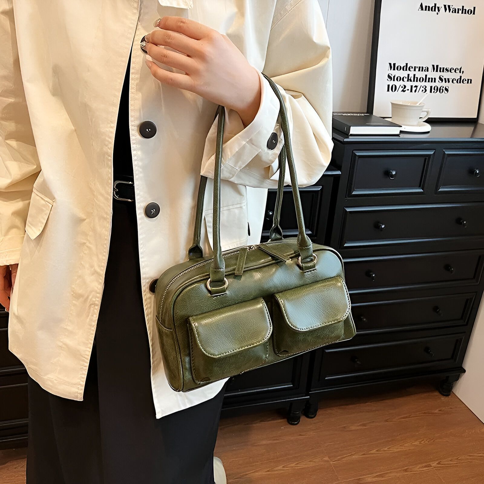 Une femme portant une veste blanche et un sac à main vert foncé avec des poches.  Le sac est devant une commode en bois noir.