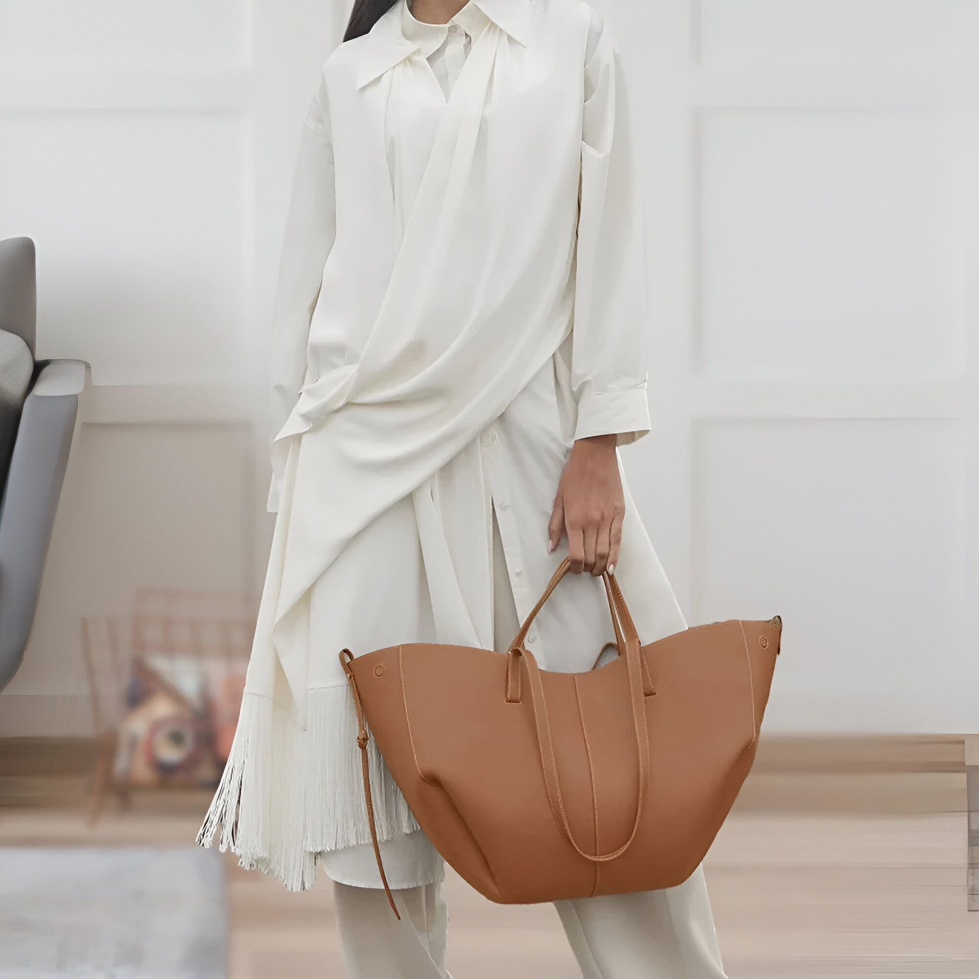 Une femme porte une robe blanche ample avec des franges et un sac à main brun en cuir.