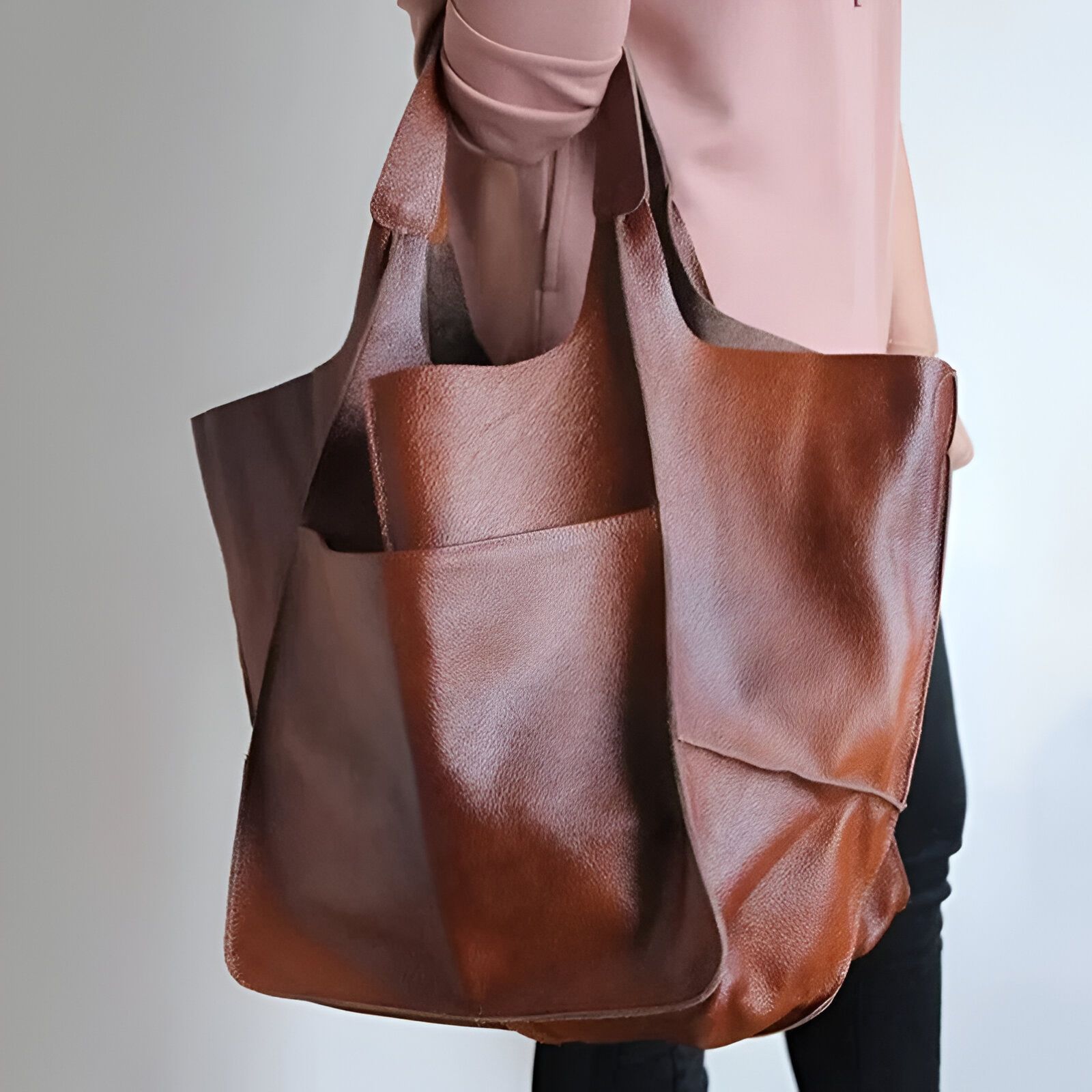 Un grand sac à main en cuir brun porté par une personne.  Le sac a des poignées en cuir et plusieurs poches.  Le sac est fait de cuir véritable.