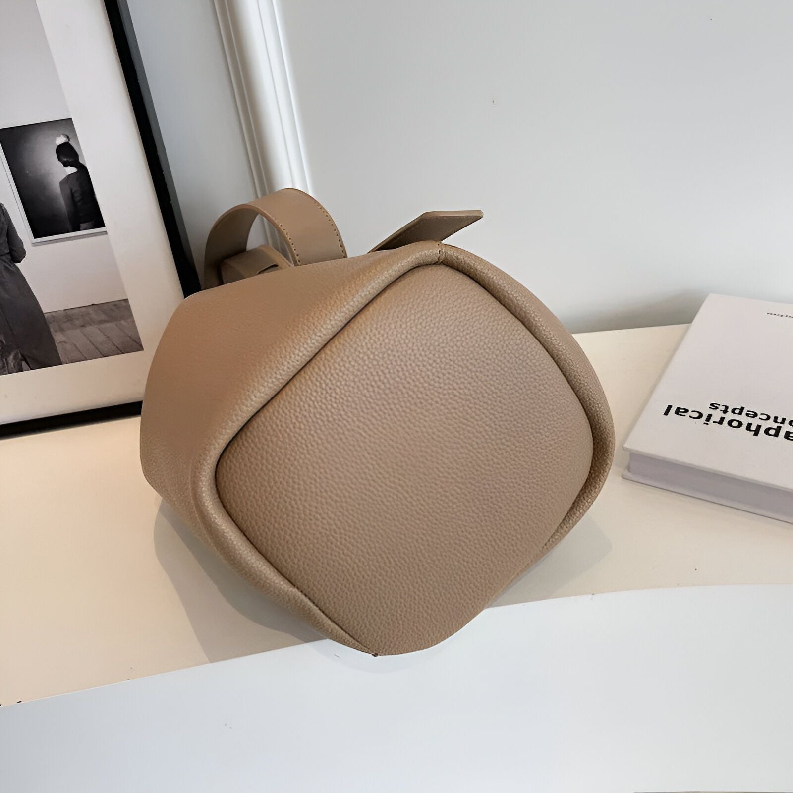 Un sac à main beige en cuir synthétique avec une anse en cuir synthétique. Le sac est de forme carrée et a une fermeture éclair sur le dessus.