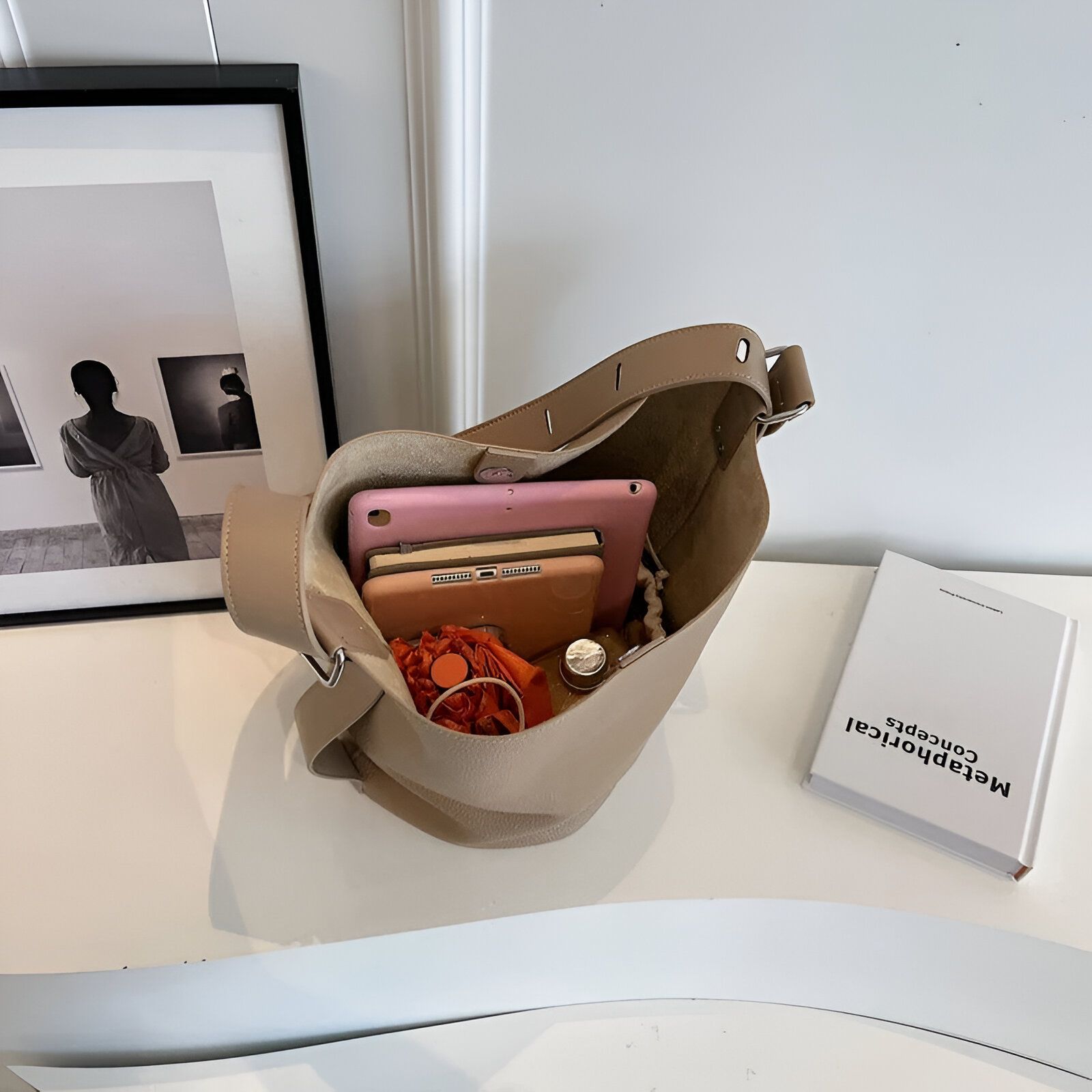 Un sac à main beige avec une tablette rose, un livre et un parapluie orange à l'intérieur.