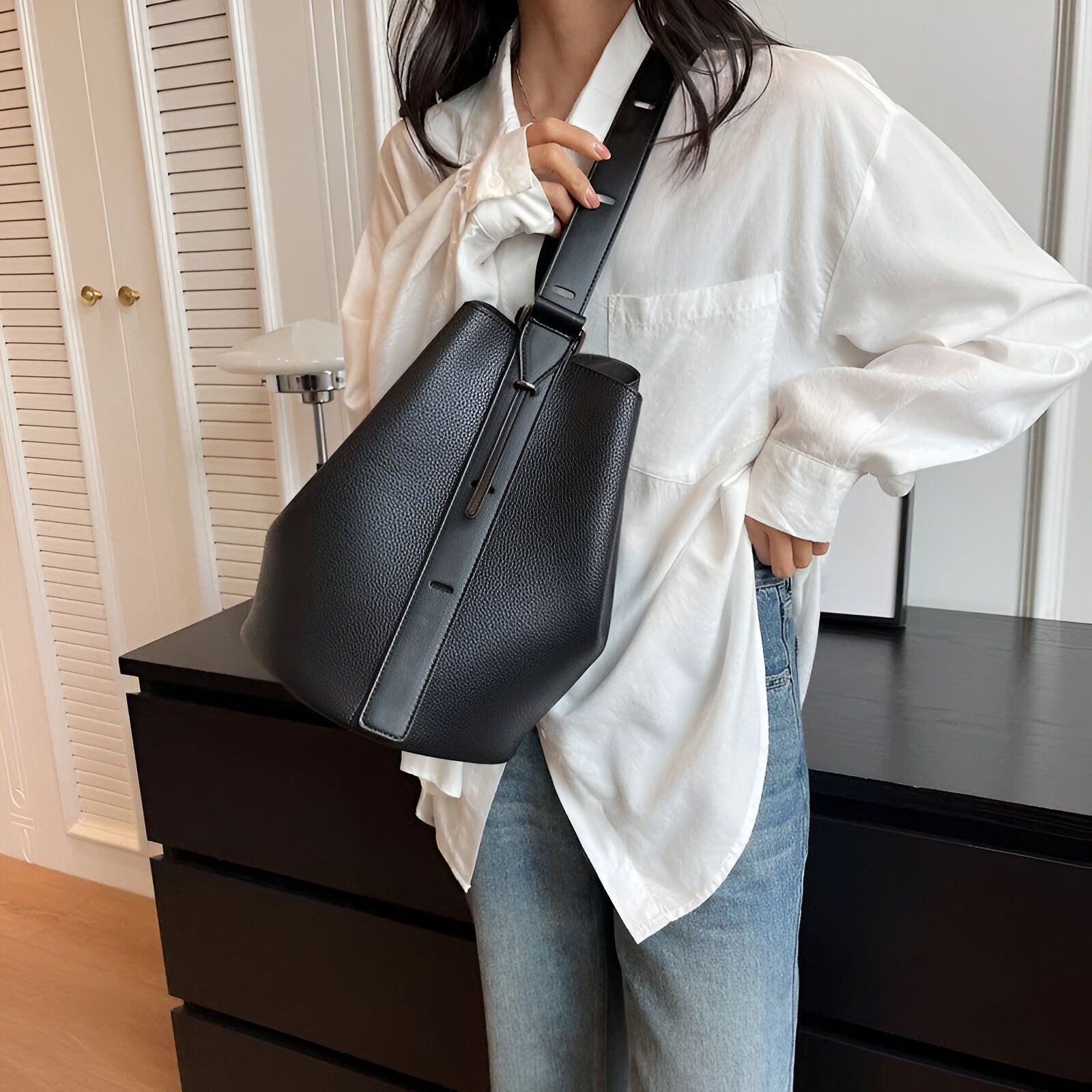 Une femme portant un chemisier blanc et un jean bleu, tenant un sac à main noir en cuir.