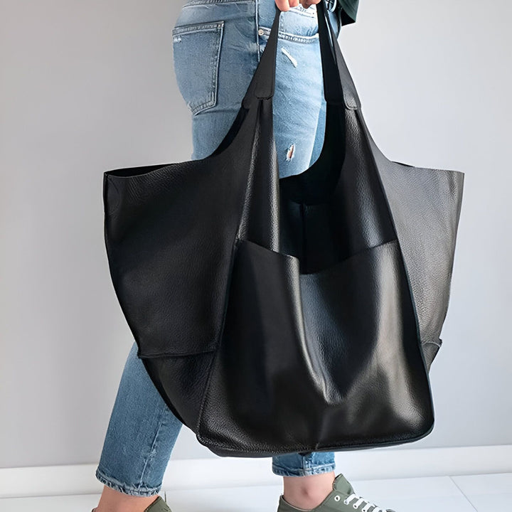 Personne portant un grand sac fourre-tout en cuir noir avec un jean et des baskets., 46193878073568,46193878106336,46193878139104,46193878171872,46193878204640