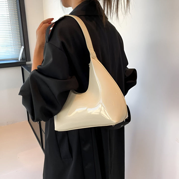Sac à main beige laqué porté épaule par une femme en manteau noir., 46193869619424,46193869652192,46193869684960,46193869717728,46193869750496
