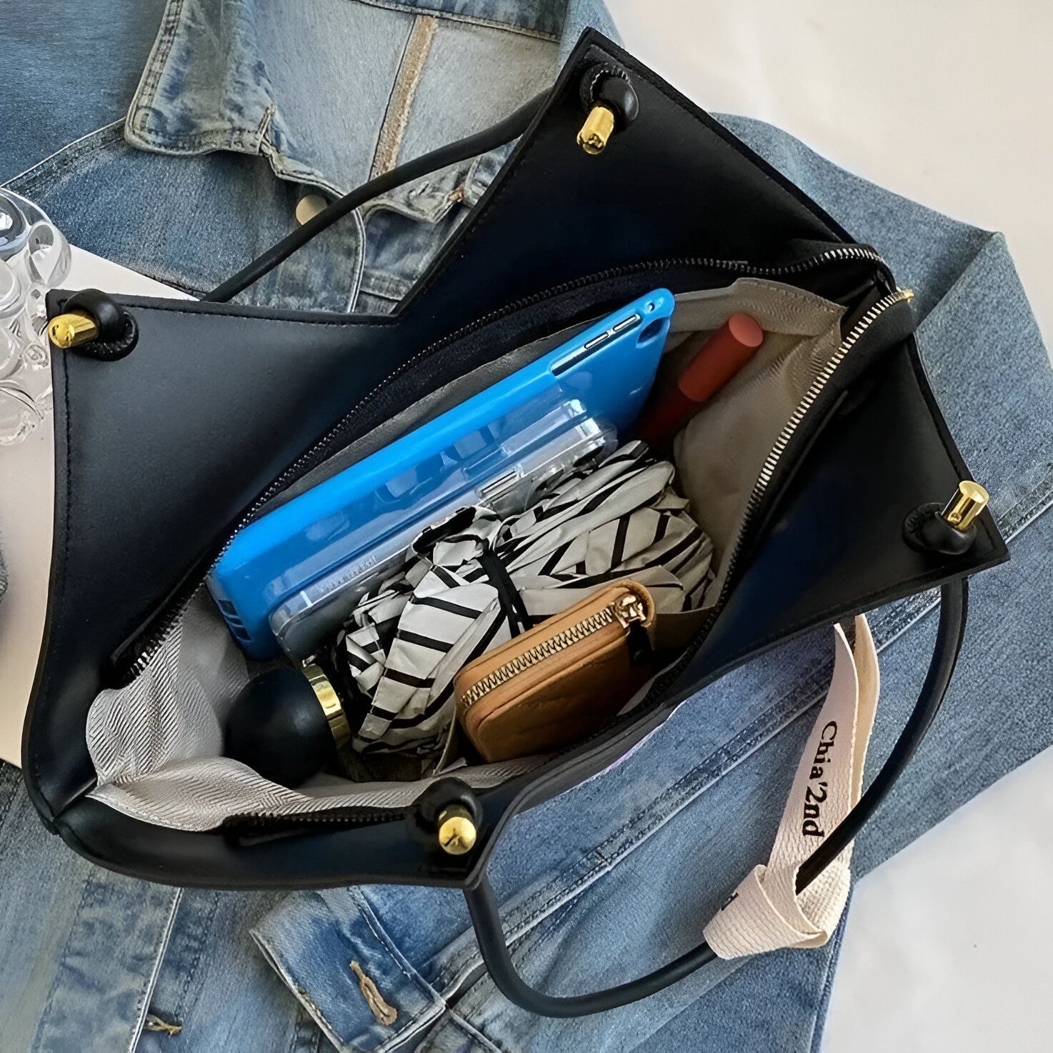 Un sac à main noir en cuir avec une tablette bleue, un parapluie pliable et un portefeuille marron à l'intérieur.