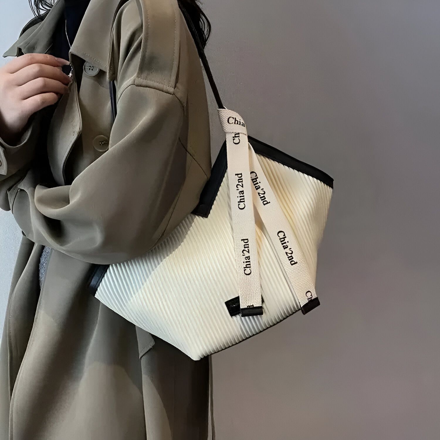 Une femme portant un manteau beige et un sac à main blanc avec des bretelles en toile portant le logo "Chia'2nd" en noir.