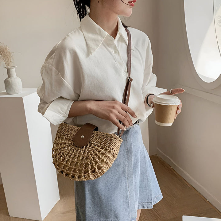 Femme tenant un café, portant une chemise blanche ample, une jupe en jean et un sac en paille., 46194029265120,46194029297888