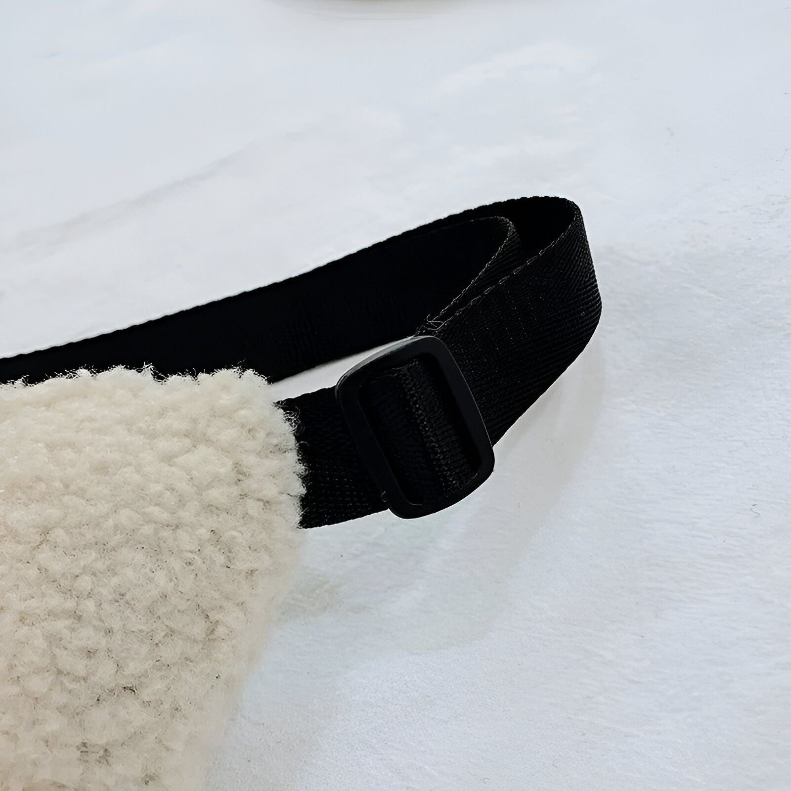 Une ceinture noire en tissu avec une boucle noire sur un sac en fourrure blanche.