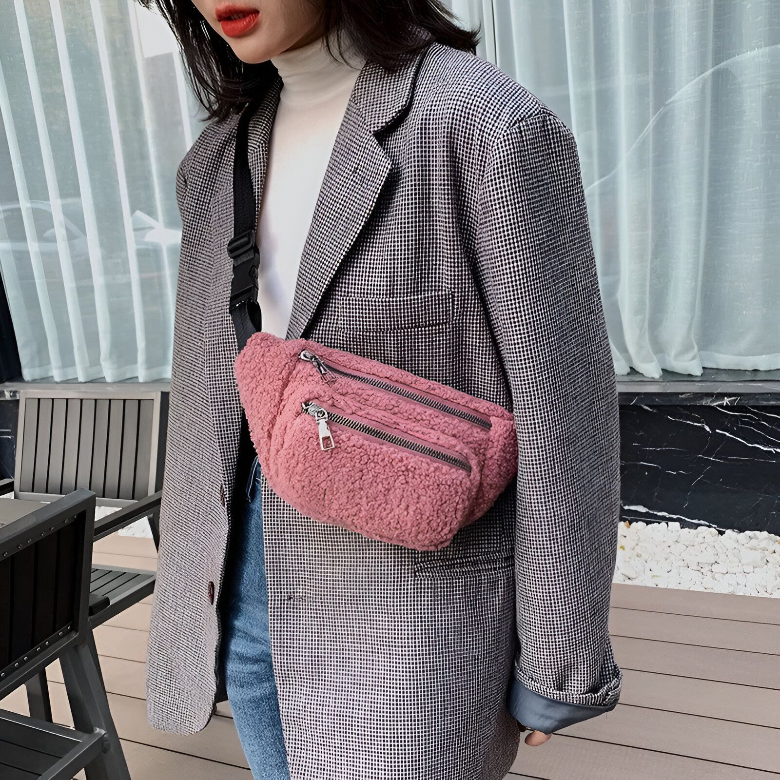 Une femme portant un blazer à carreaux gris et un sac banane rose en fourrure.