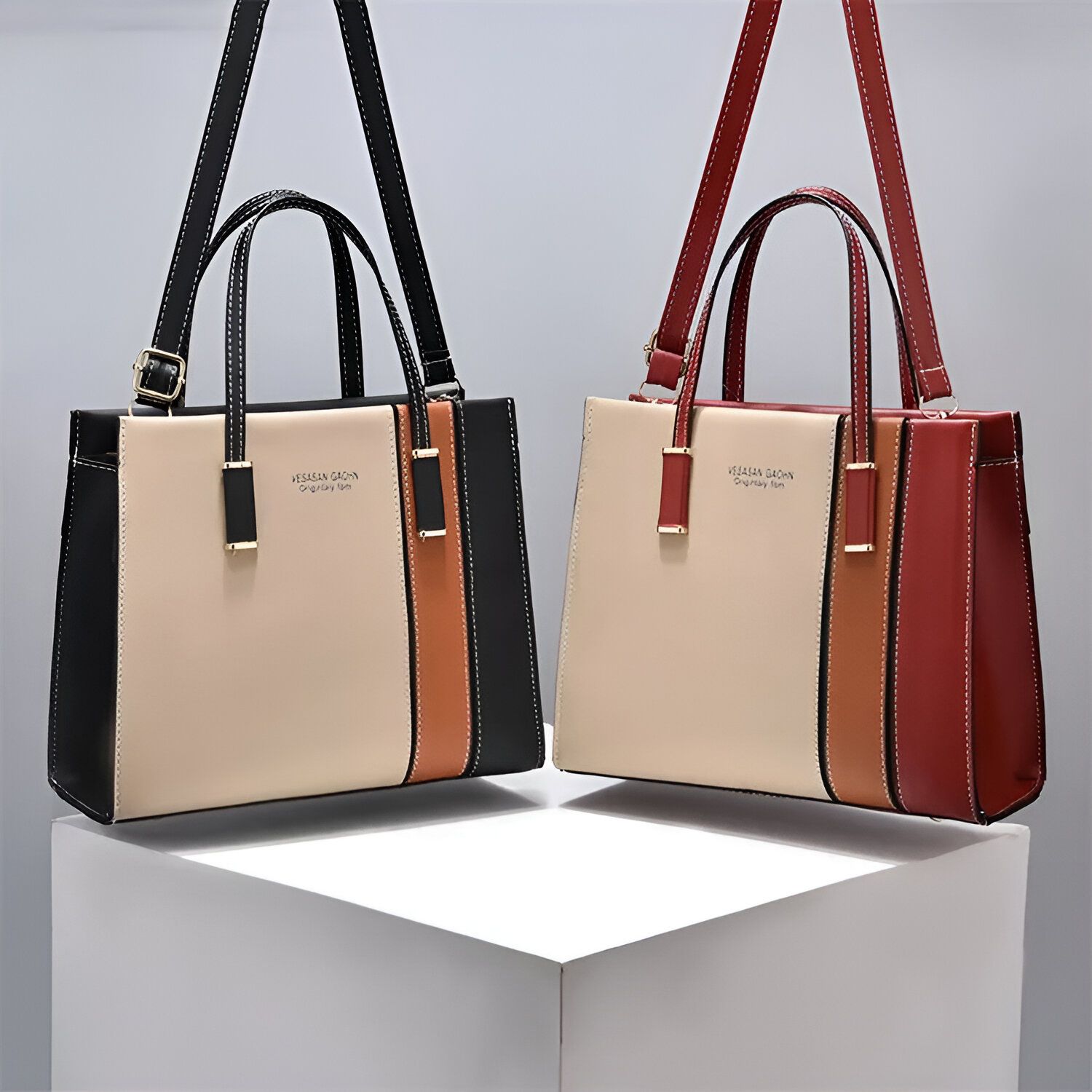 Deux sacs à main en cuir de couleur beige, noir et rouge, avec des anses et une bandoulière. Les sacs sont posés sur un cube blanc.