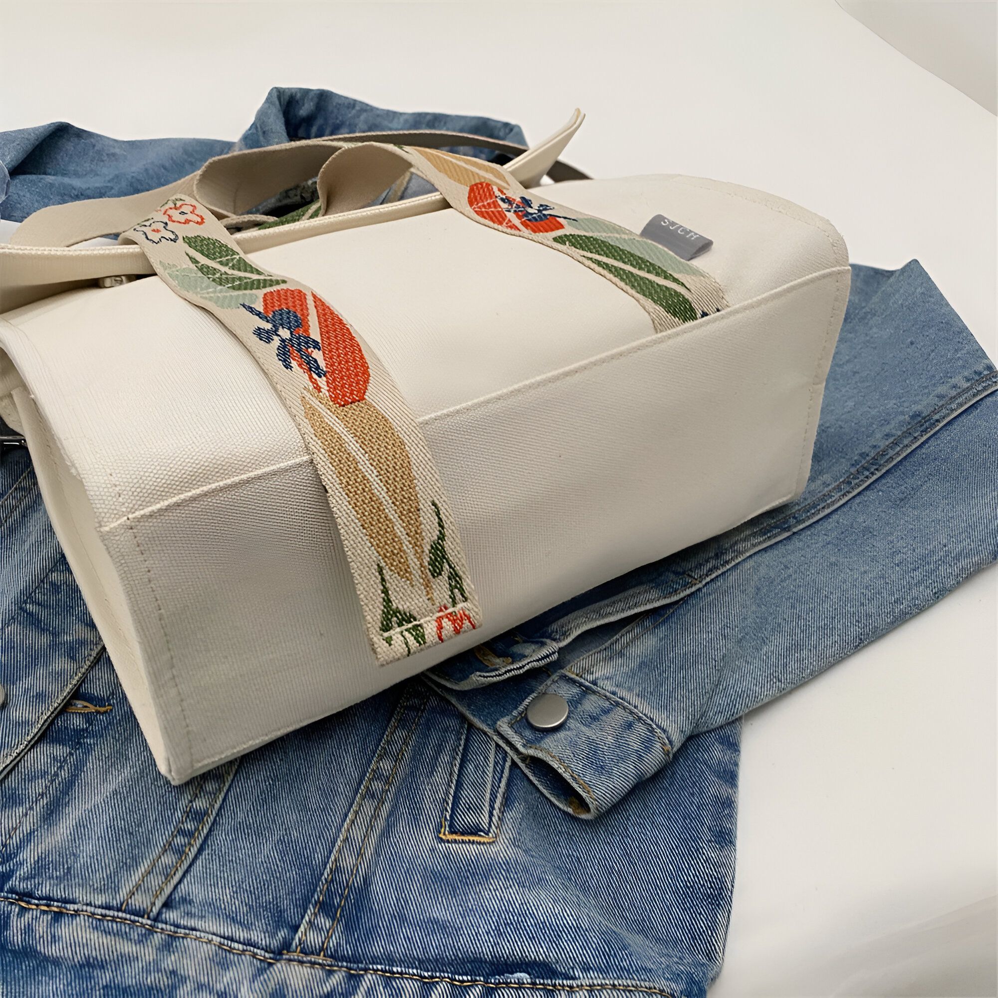 Un sac à main en toile blanche avec des anses à motifs floraux sur une veste en jean bleue.