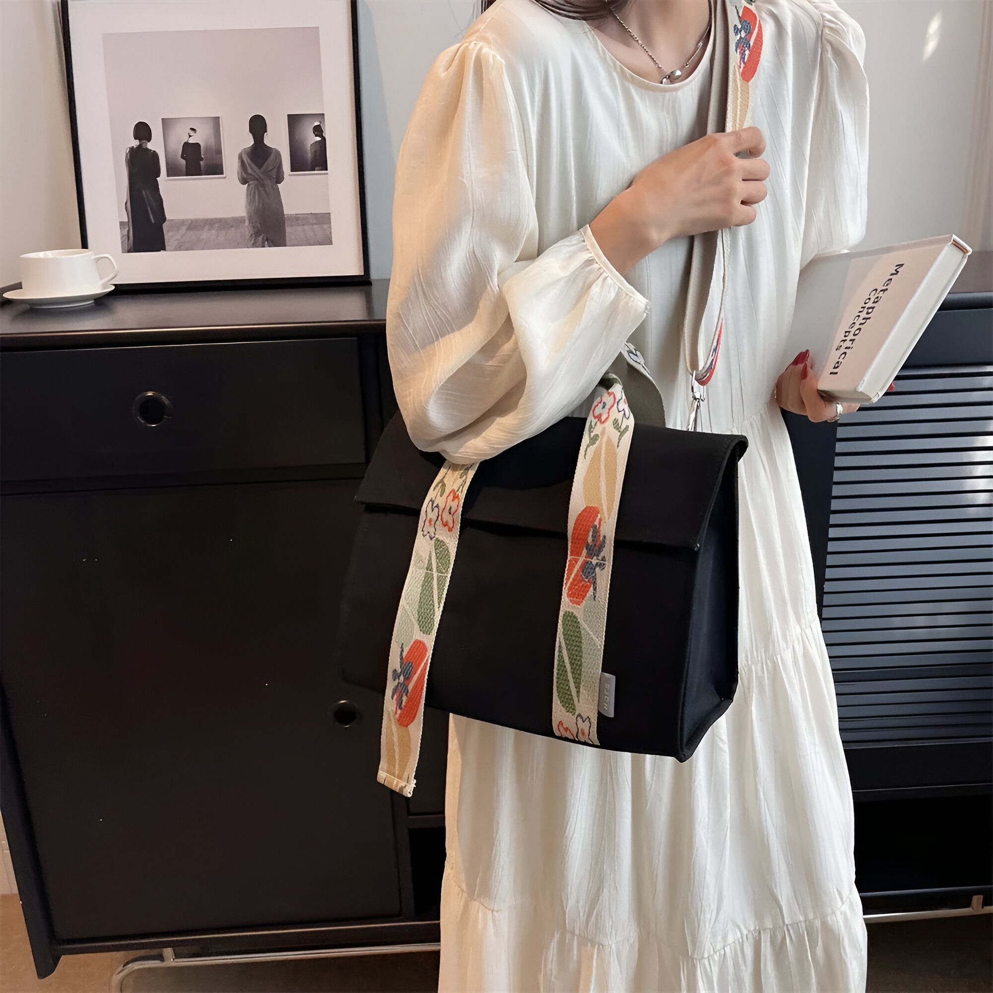 Une femme portant une robe blanche et un sac à main noir avec des bretelles à fleurs.