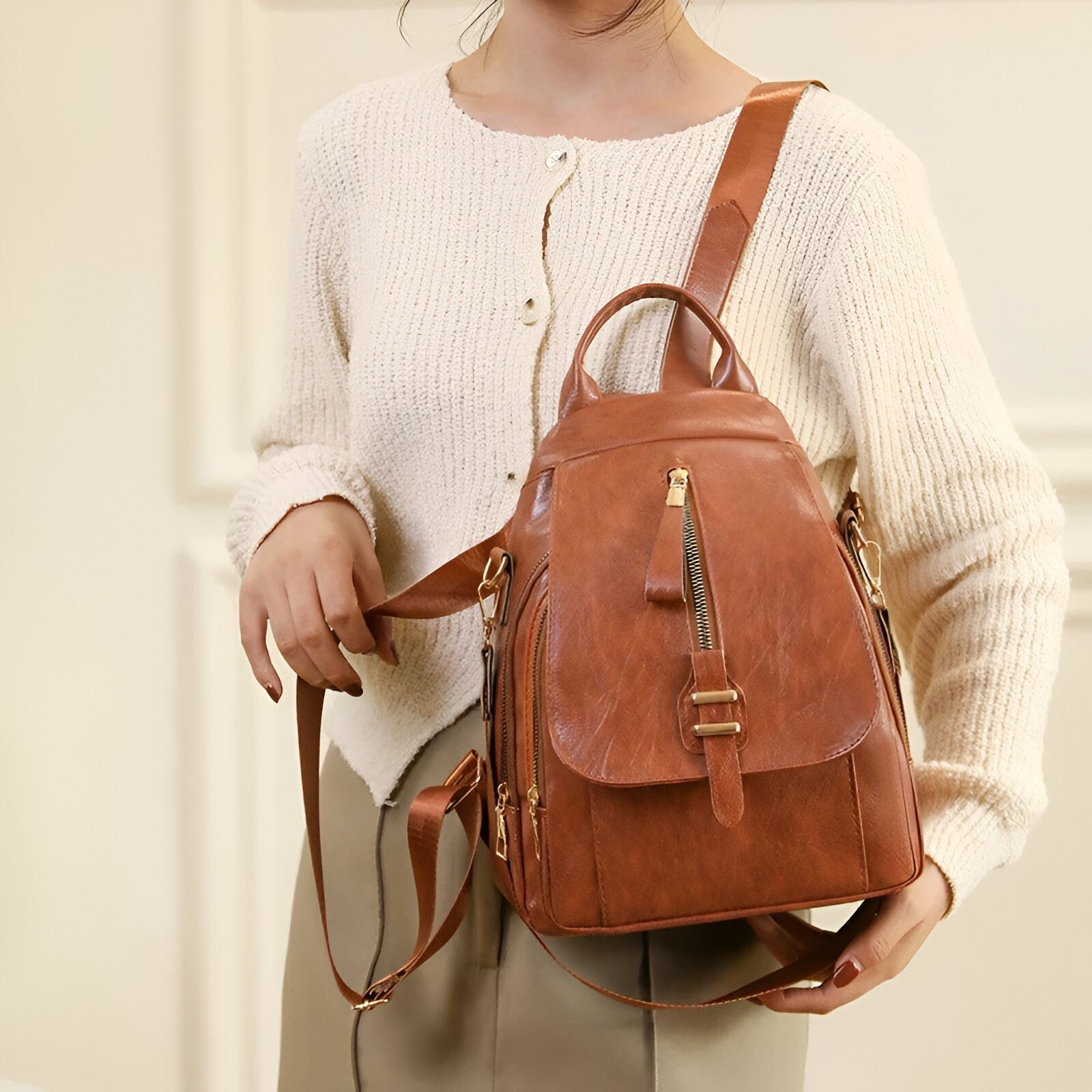 Une femme portant un sac à dos en cuir marron clair.  Le sac à dos a des fermetures éclair dorées et une sangle ajustable.