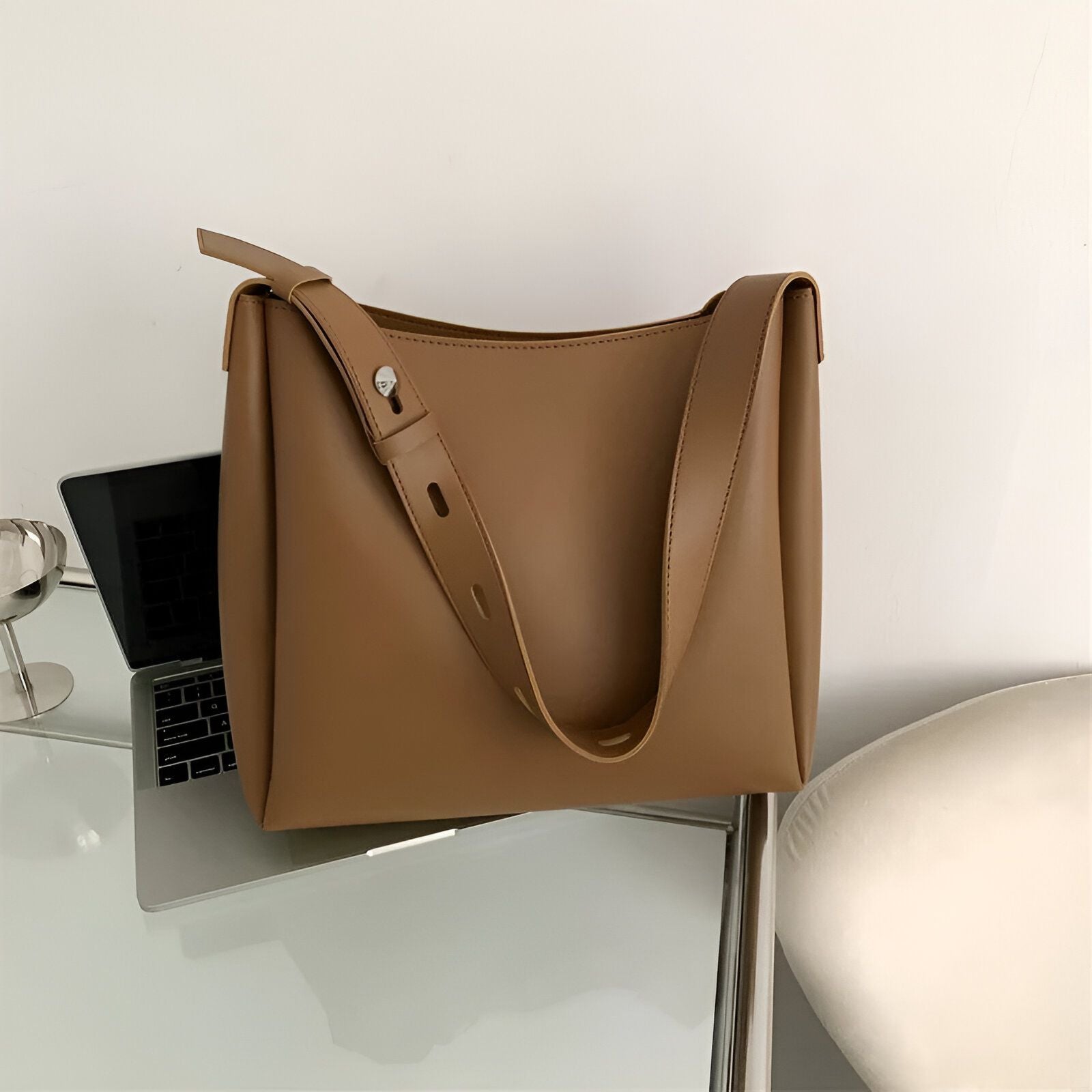 Un grand sac à main brun en cuir sur une table en verre.