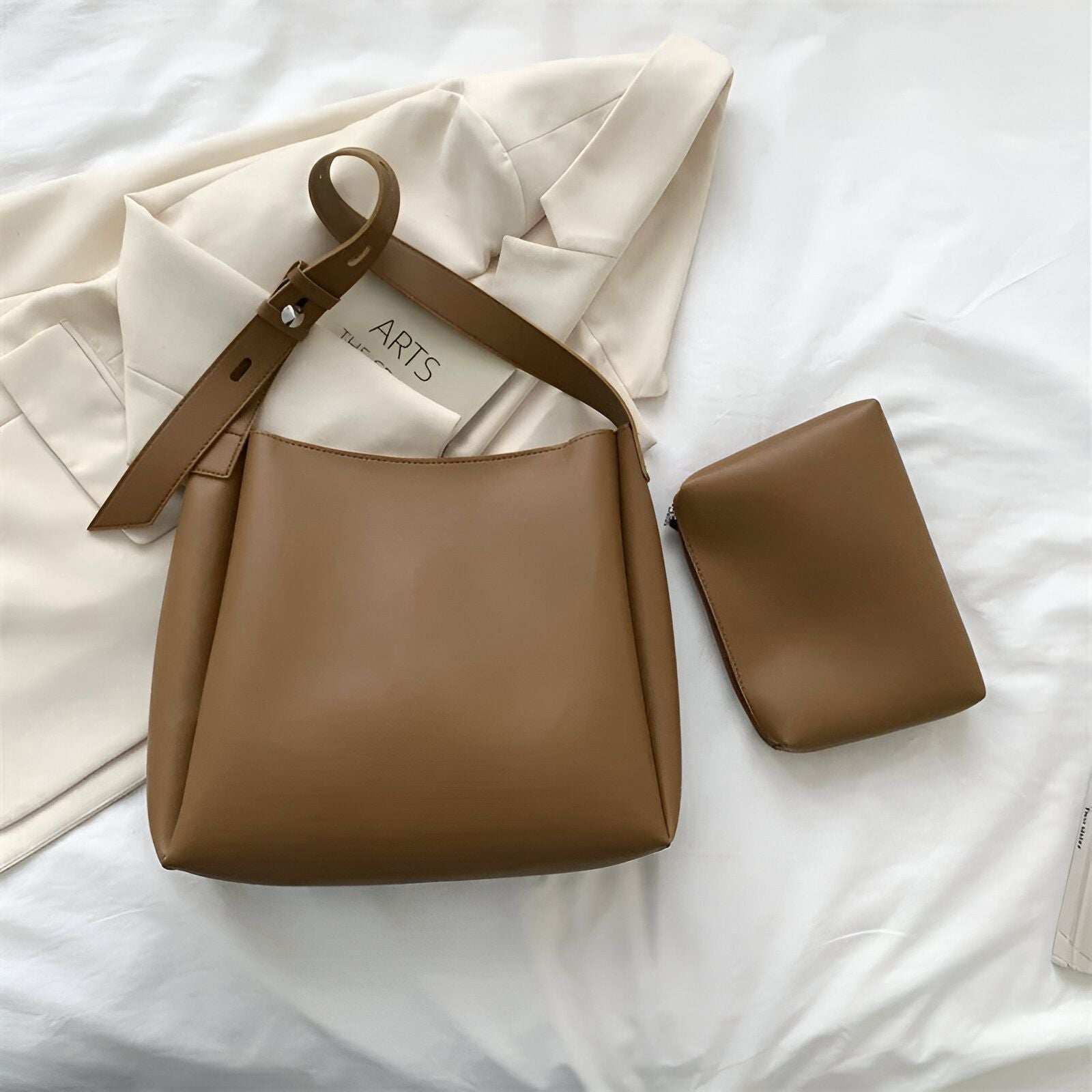 Un grand sac à main brun avec une petite pochette assortie sur un lit blanc.