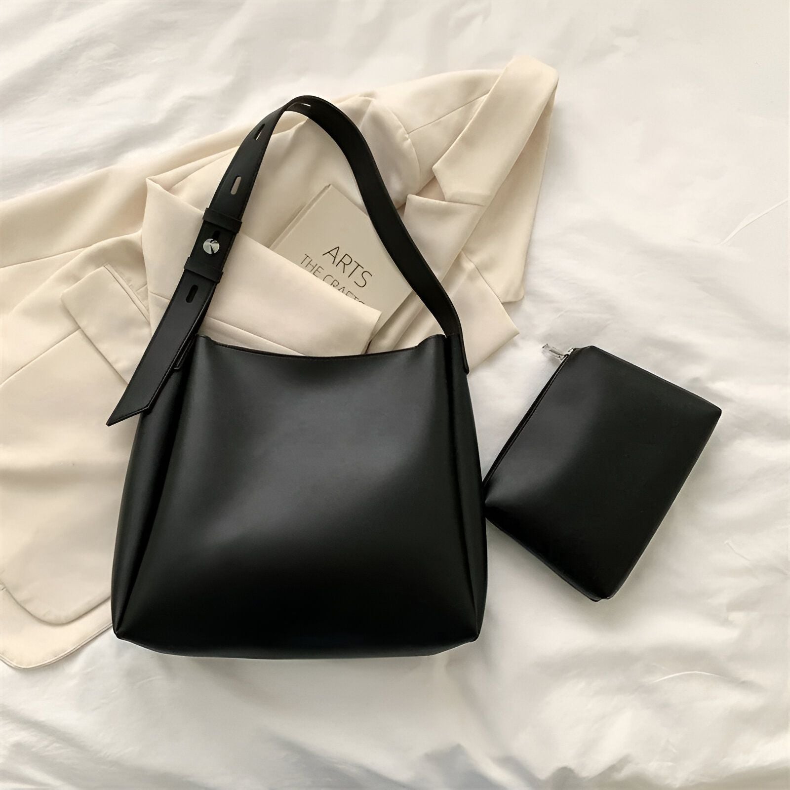 Un sac à main noir avec une petite pochette assortie, posé sur un lit blanc.