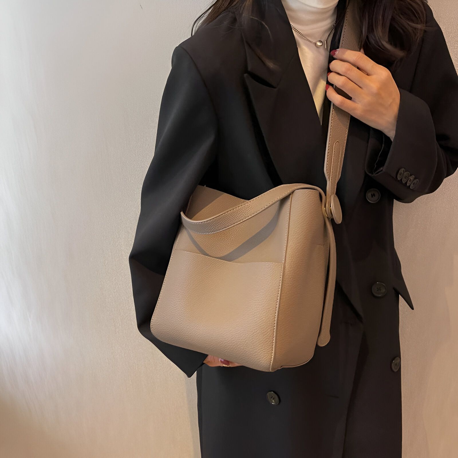 Une femme portant un manteau noir élégant et un sac à main en cuir beige.