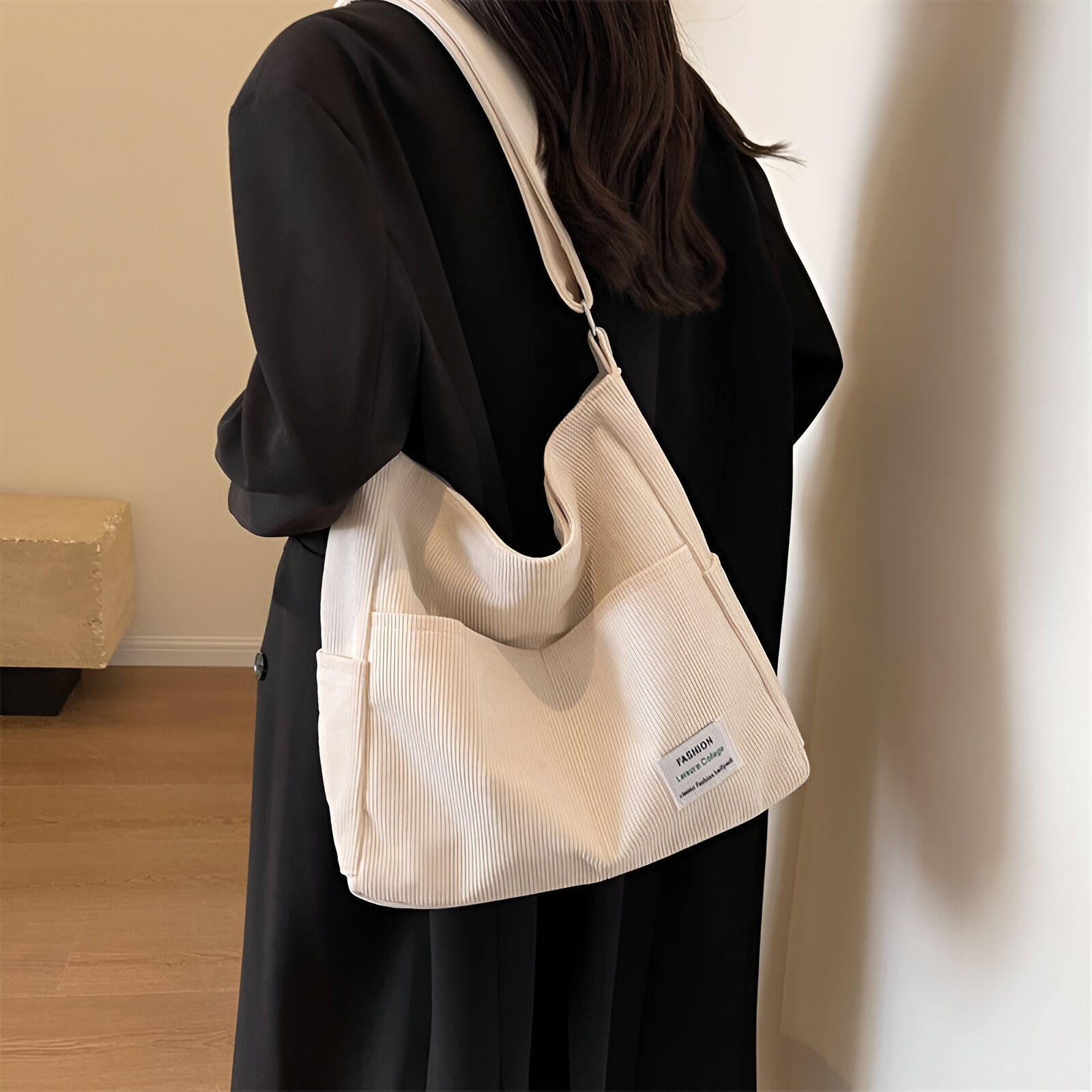 Une femme portant un sac à main blanc en bandoulière. Le sac est en tissu côtelé et a une poche avant avec un logo "Fashion" en noir.