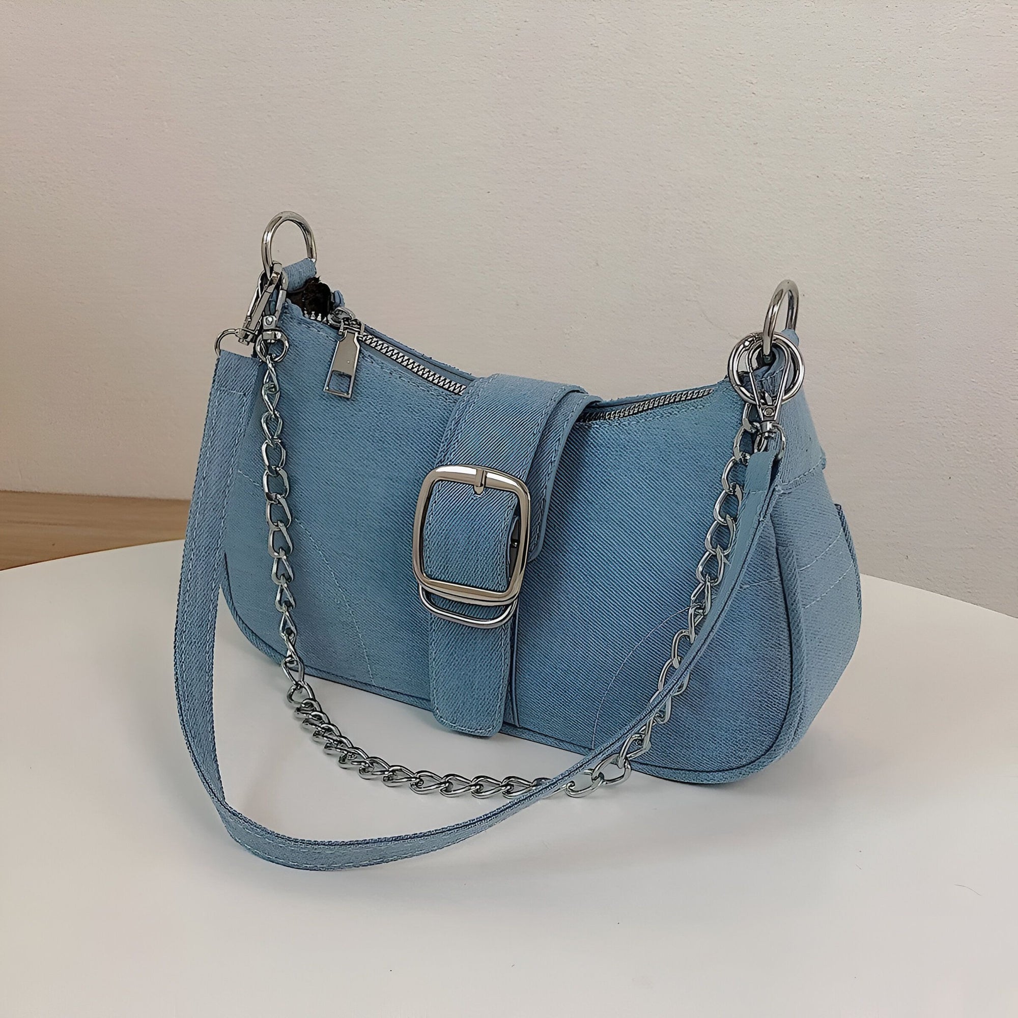 Un sac à main bleu en jean avec une chaîne argentée et une boucle.