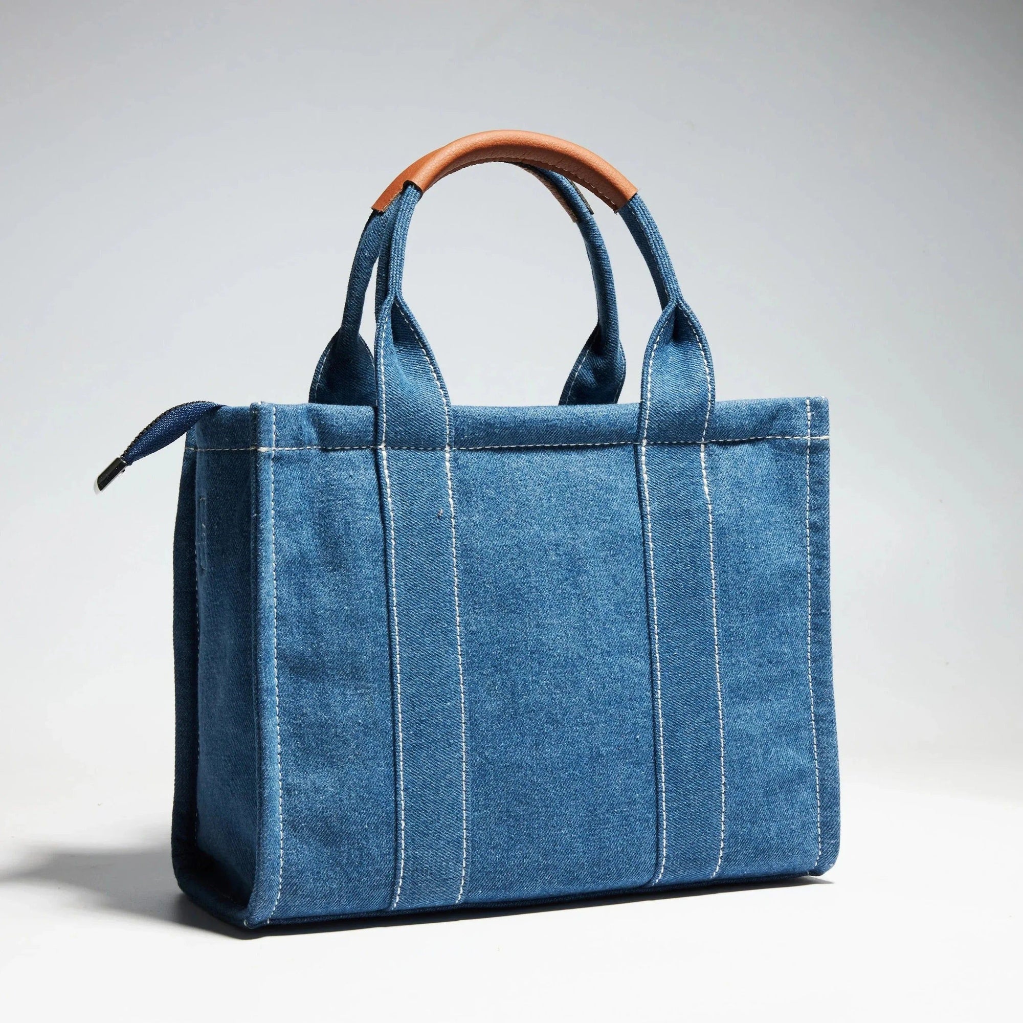 Un sac à main en jean bleu avec des poignées en cuir marron.