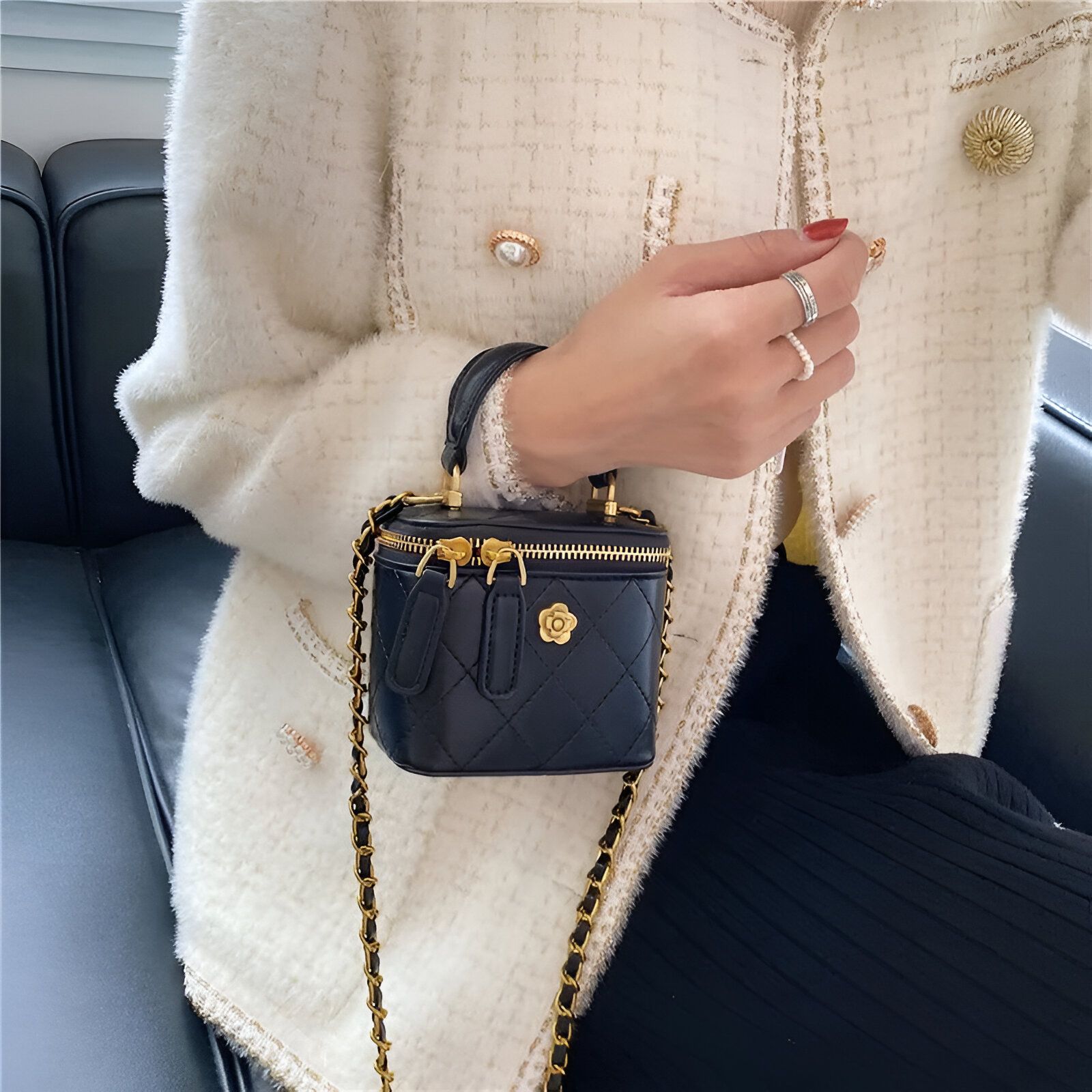 Un petit sac à main noir avec une chaîne dorée porté par une femme vêtue d'un blazer blanc à motifs.