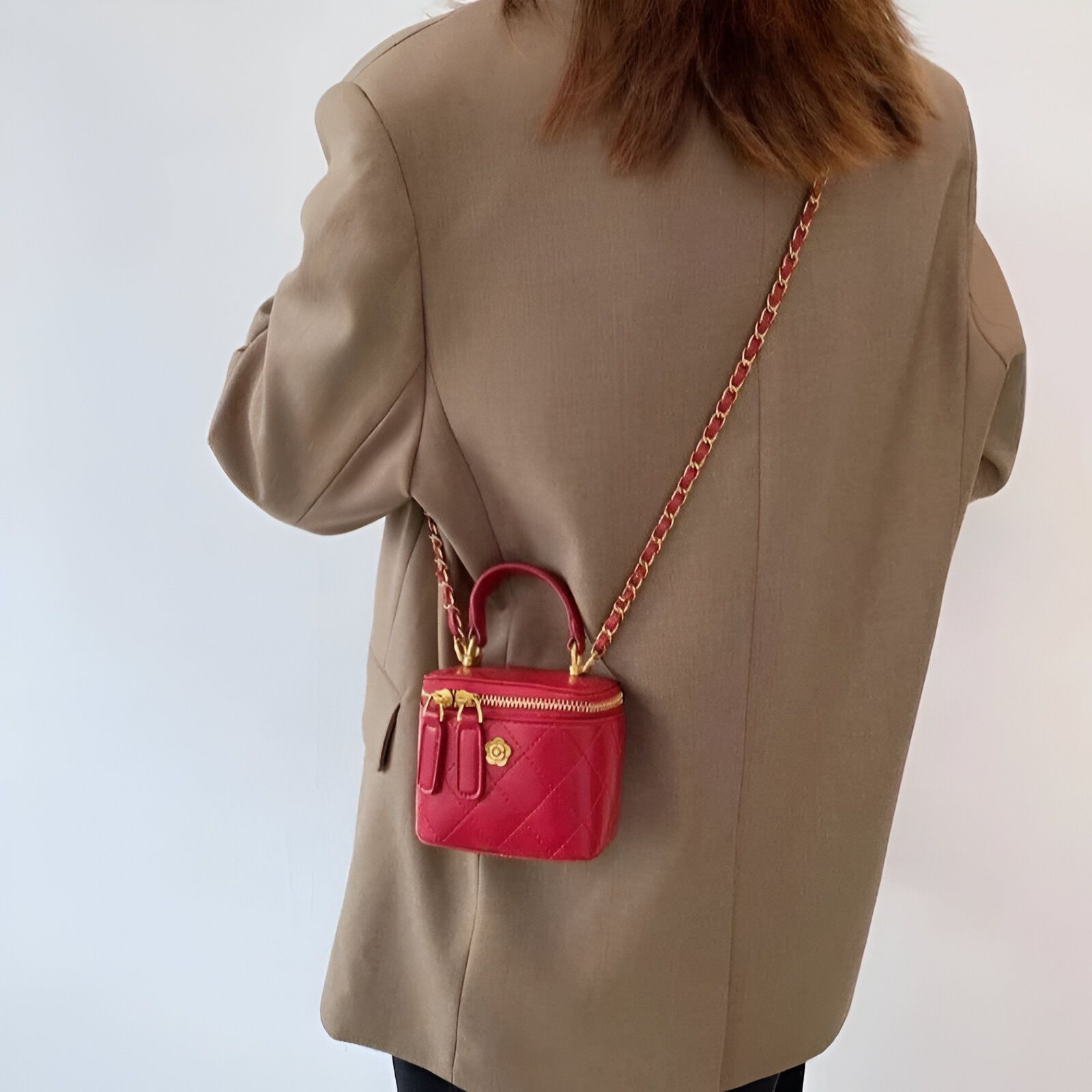 Une femme portant un blazer marron et un petit sac à main rouge avec une chaîne dorée.