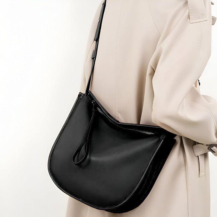 Sac bandoulière noir en cuir porté par une personne en trench beige., 46193866113248