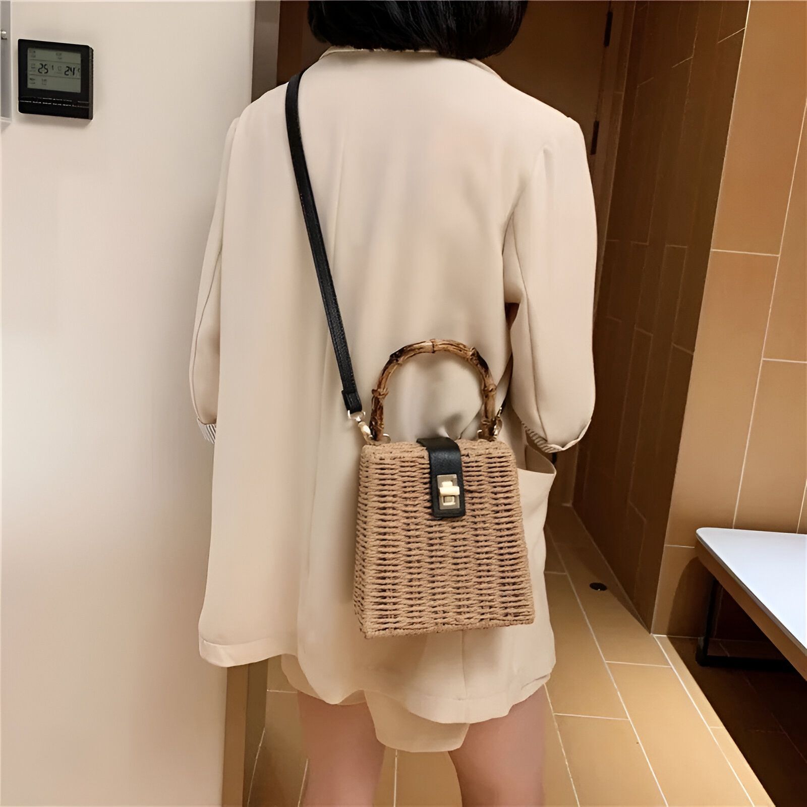 Une femme portant un blazer beige et un sac à main en paille avec une anse en bambou.