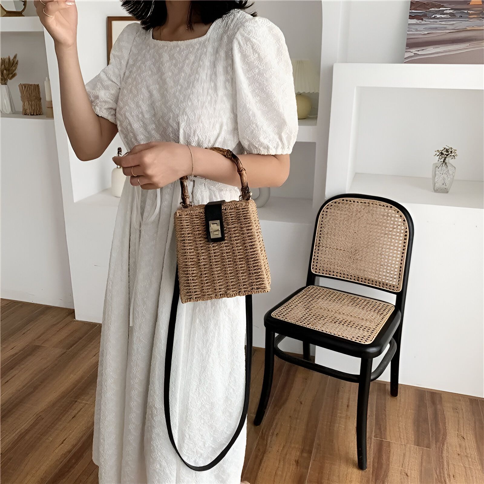 Une femme en robe blanche tient un sac à main en osier avec une poignée en bambou.  Le sac est de couleur beige et est porté sur l'épaule.