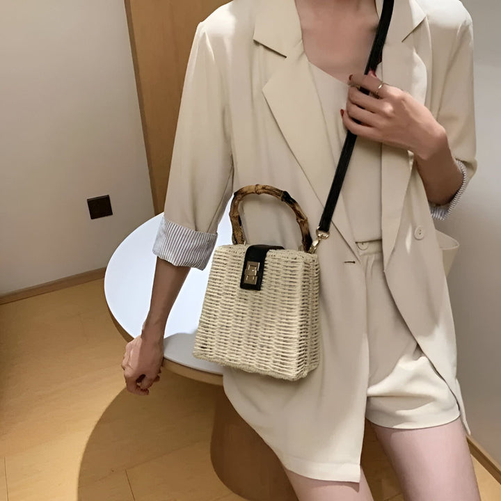 Sac en paille carré avec poignées en bambou et bandoulière noire, porté par une personne en tenue beige., 46193945510112,46193945542880